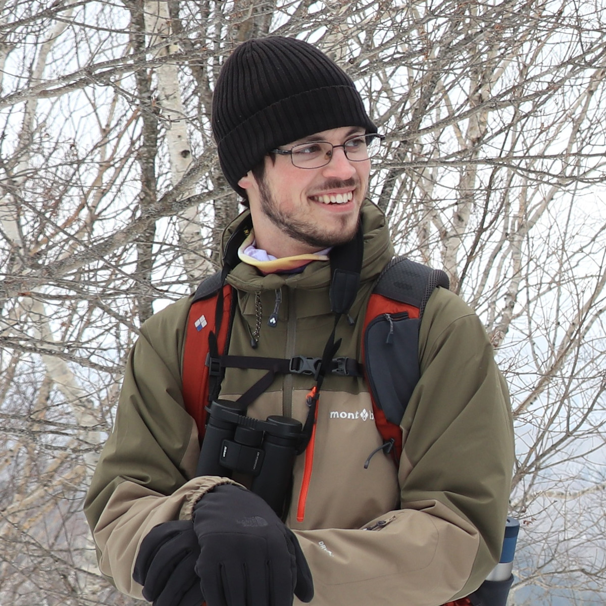 Adventure Hokkaido guide Zac stands in front of birch trees. It's winter and the trees have no leaves.