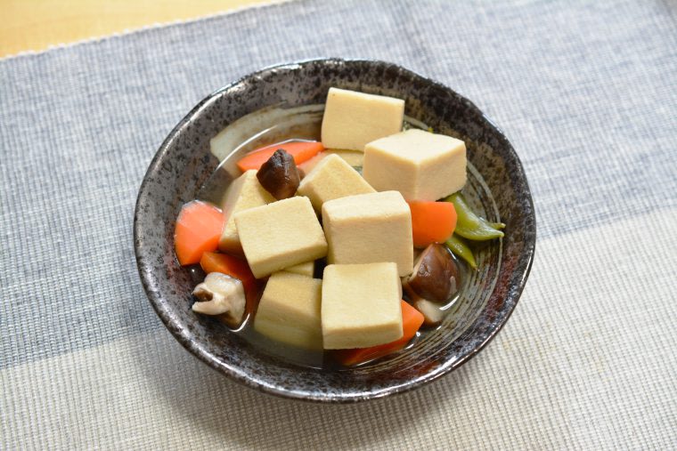 A dish of simmered tofu and vegetables such as mushrooms, carrots and sugar snap peas.