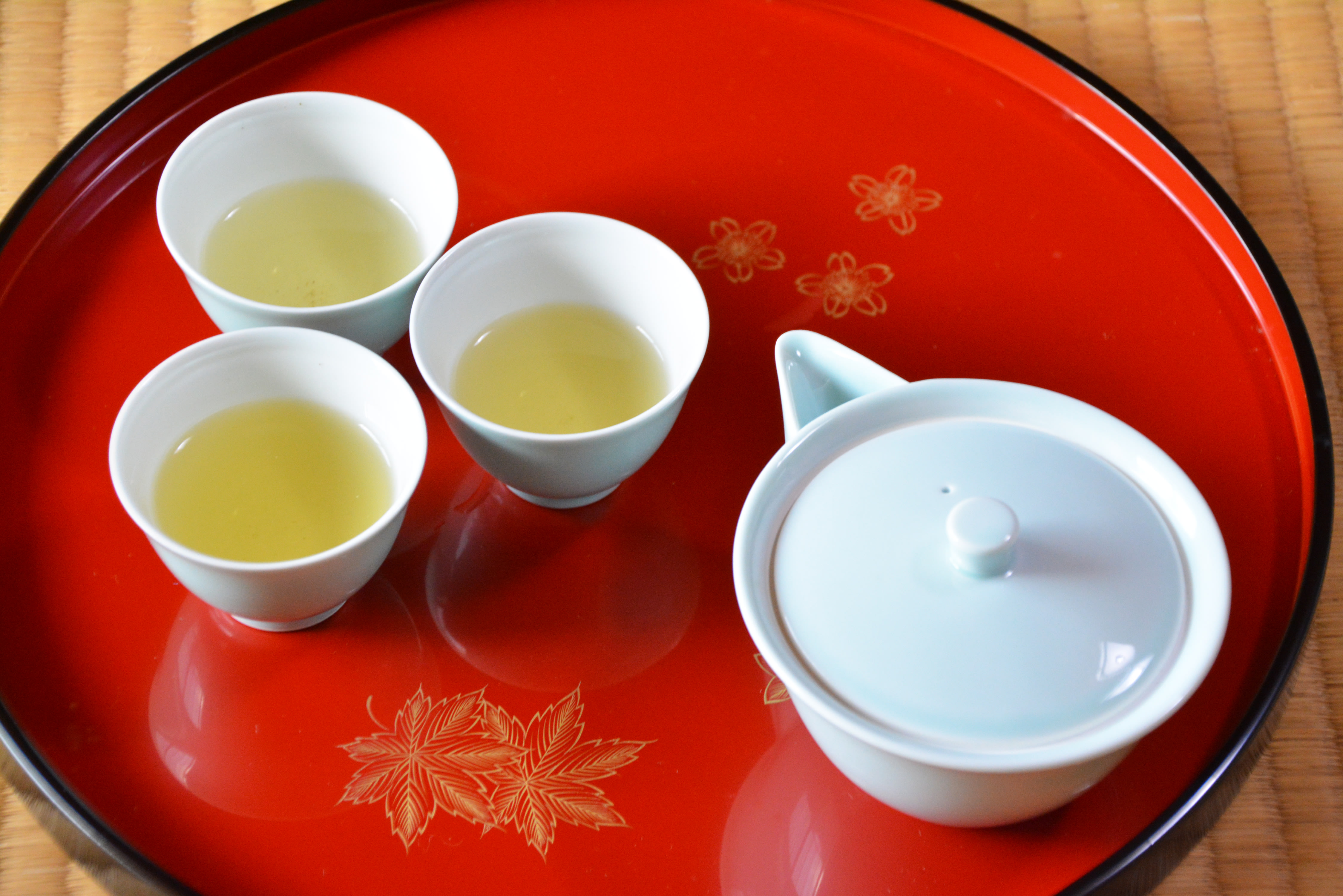 A Japanese teapot sits on a red tray with three cups of tea. The cups have green tea in them.