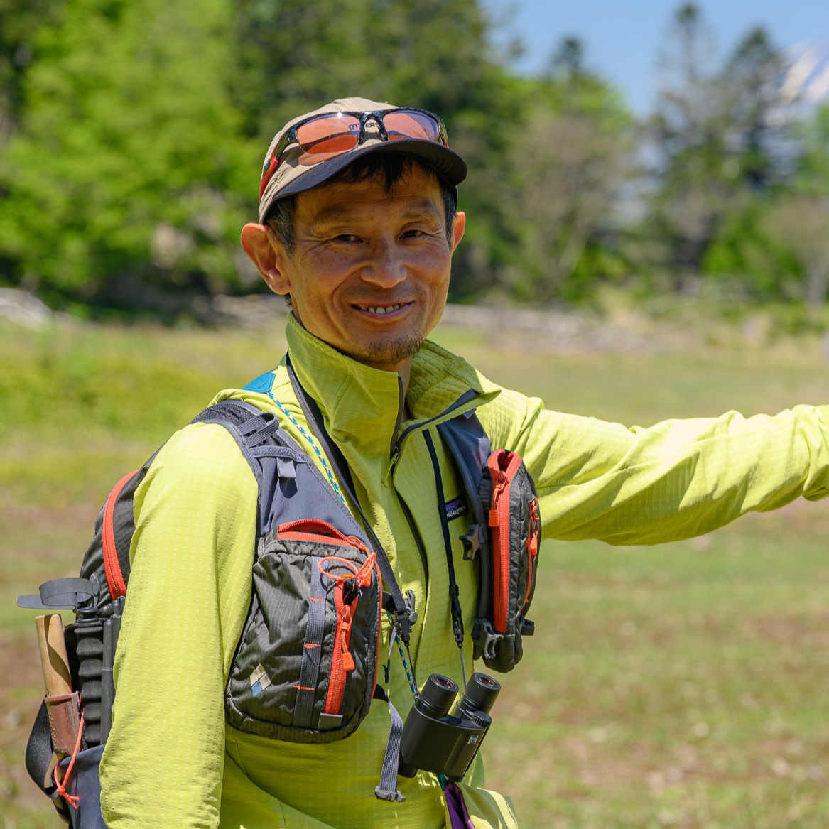 Adventure Hokkaido guide Gen poses at Daiheigen on Nakajima Island, Lake Toya. In the background, the summit of Mt. Yotei rises in the gap between green trees and blue sky.