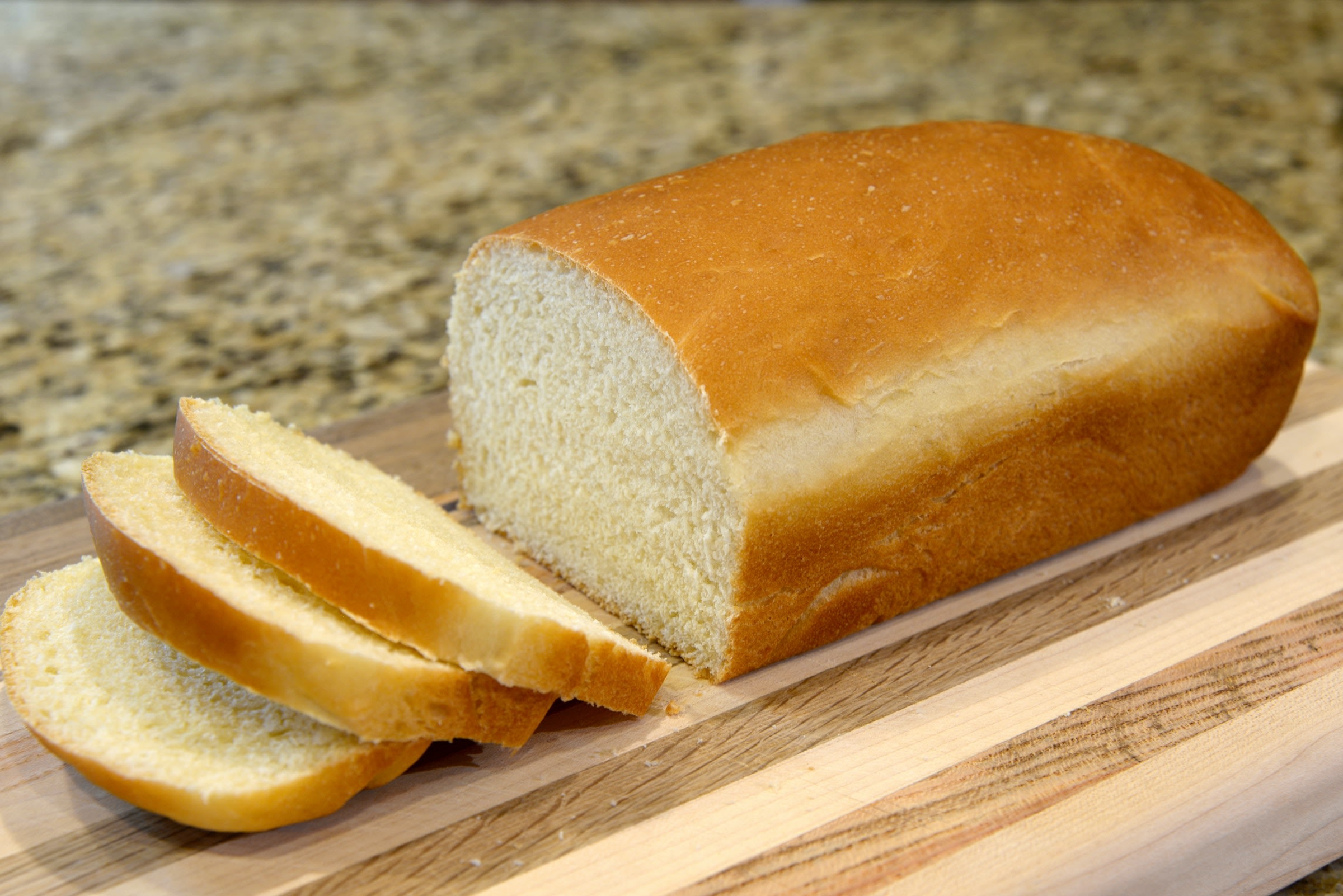 A loaf of white bread on a cutting board with three slices cut away.