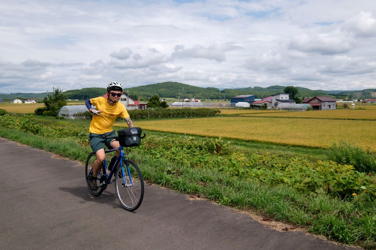 A cyclist poses for a photo as he rides alongside golden rice fields