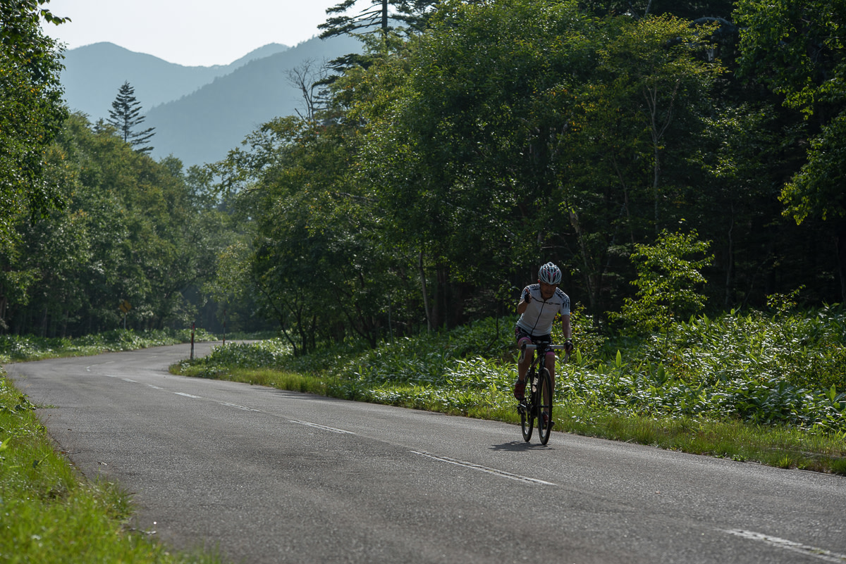 A cyclist waves as high climbs a rural road