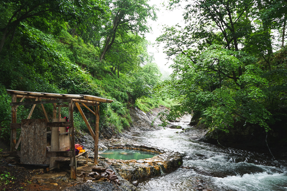 A hot-spring pool sits next to a wild river surrounded by greenery