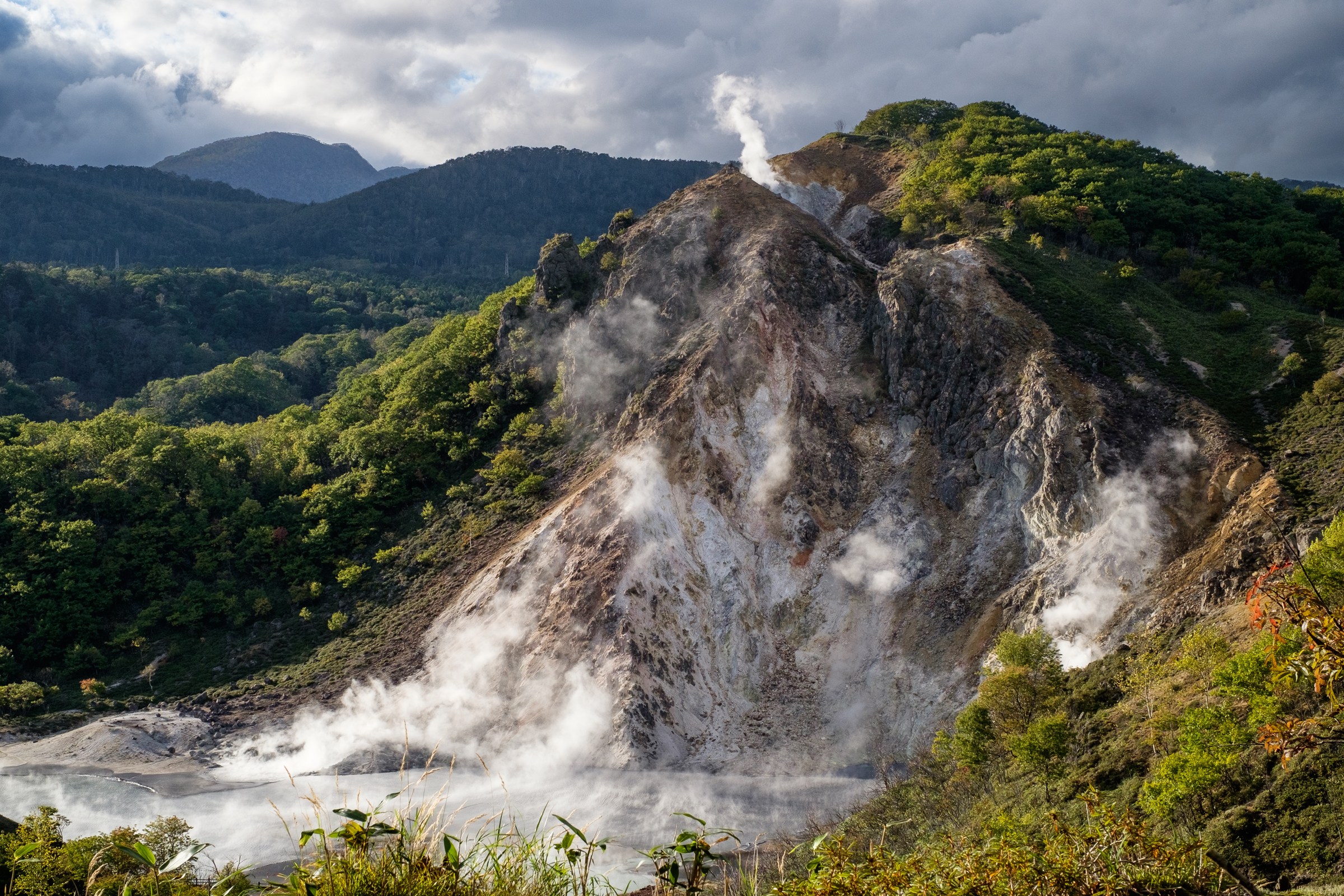 A view of Oyunuma Pond in Noboribetsu Hell Valley. The pond lies at the bottom of a volcanic fumarole, from which steam rises into the air.