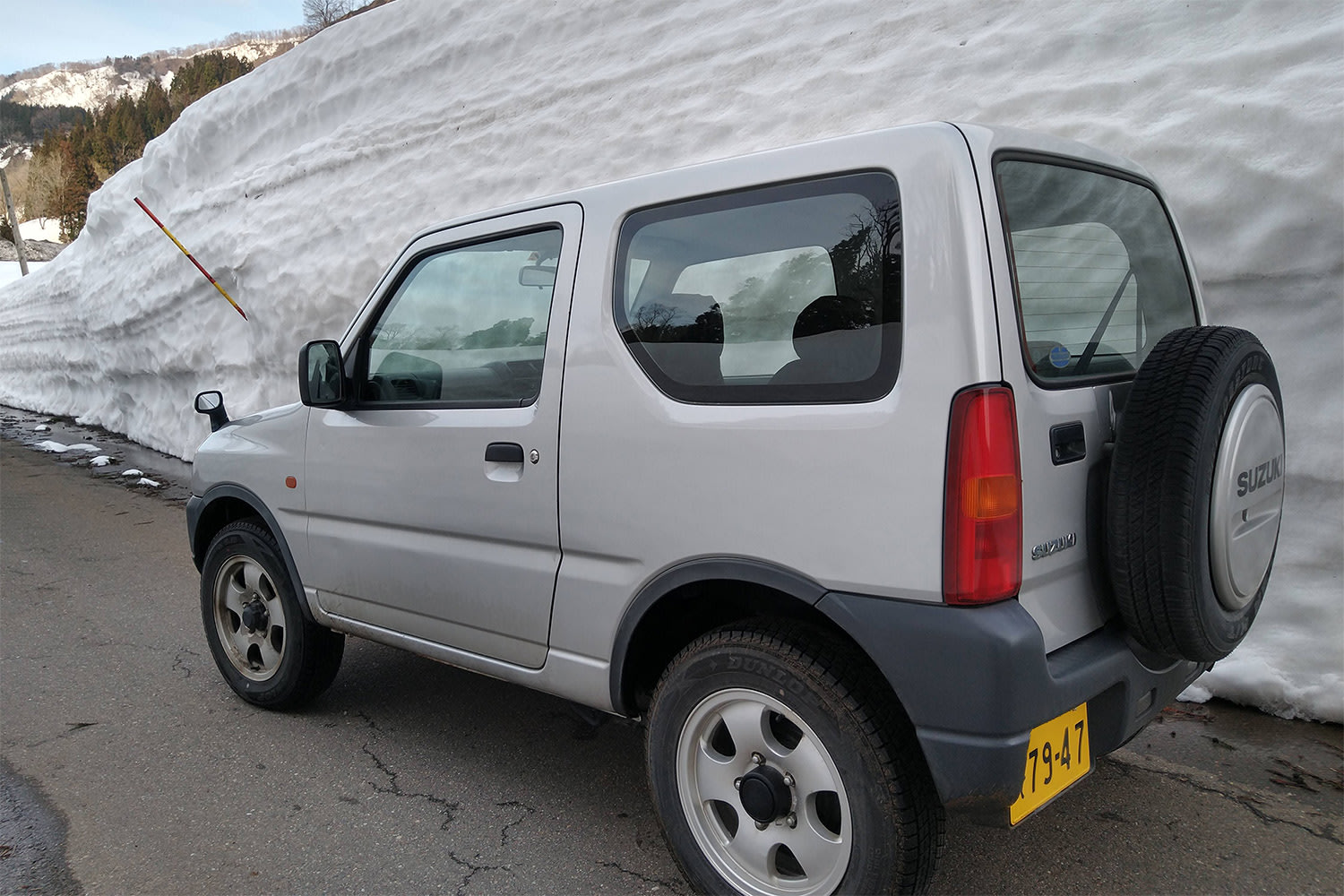 A Japanese compact car is surrounded by walls of snow that are taller than the car
