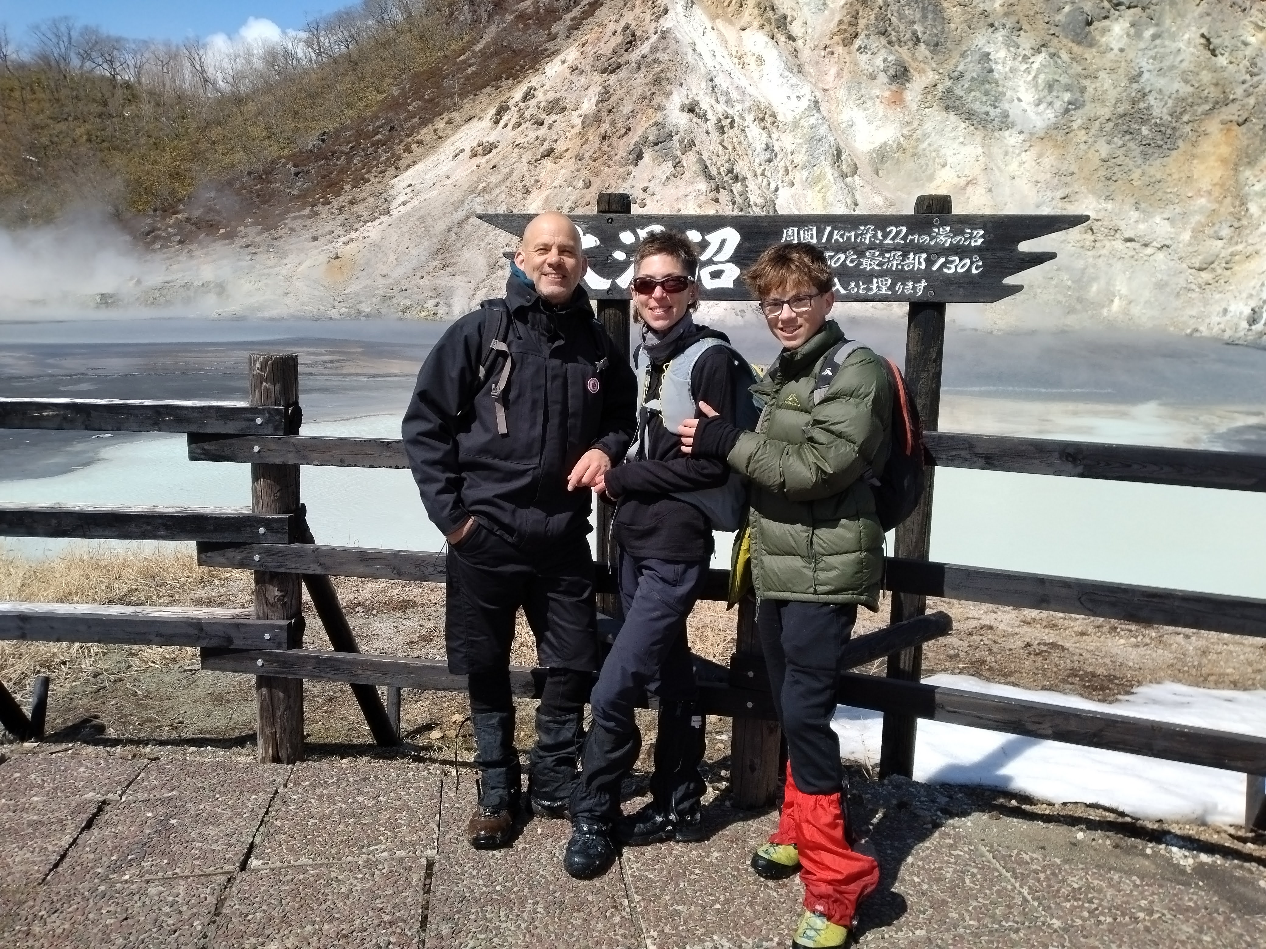 Three guests pose in front of Oyunuma while steam rises in the morning light.