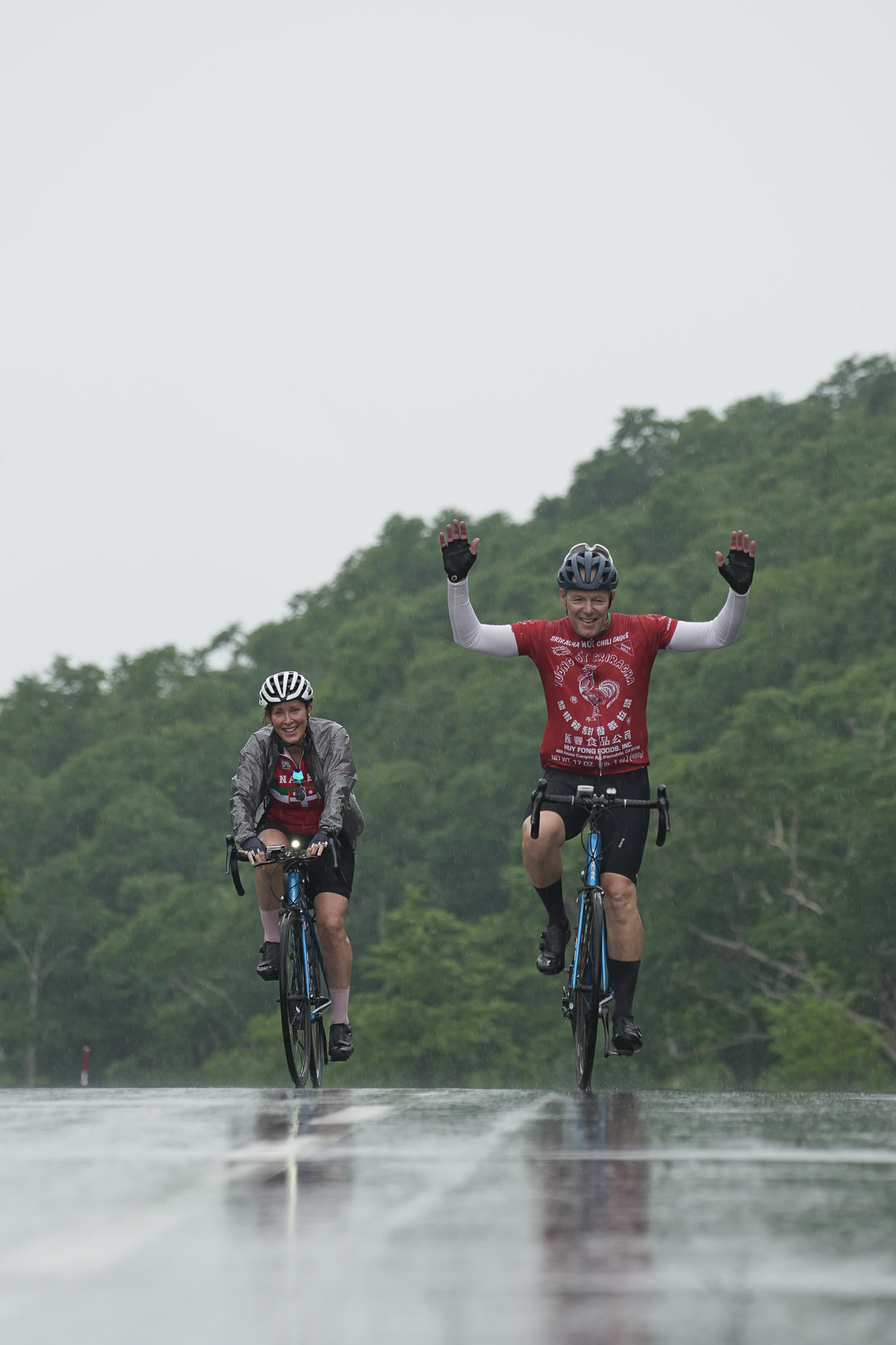 Two cyclists raise their hands as they cycling through the pouring rain.