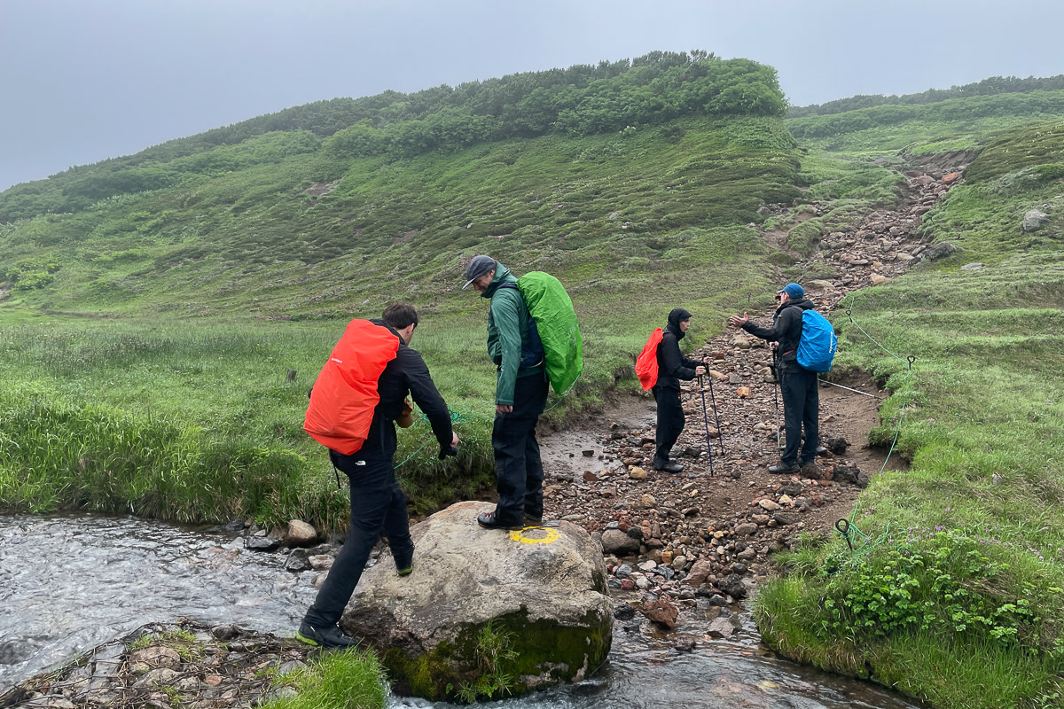 A hiking guide helps guests across a stream in the Daisetsuzan National Park