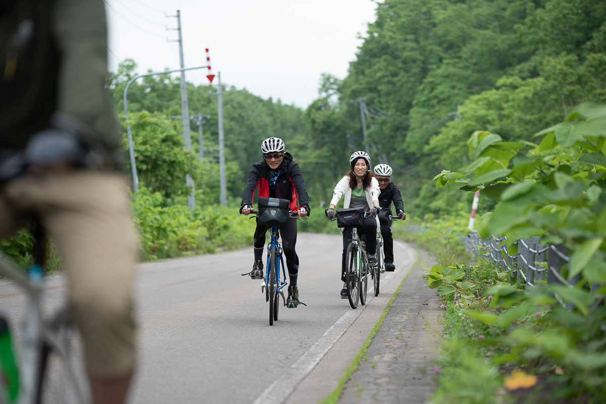A guided cyclist group rides along a quiet rode flanked in greenery.