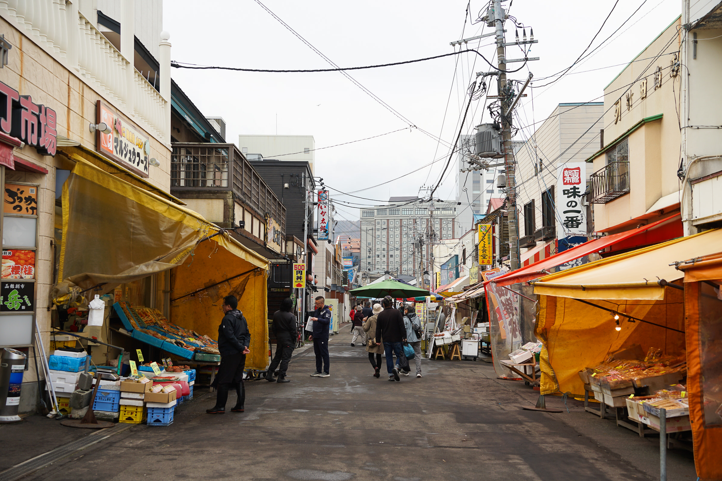 A road at Hakodate Morning Market. Large tarpaulin stands line the street, sheltering today's produce.