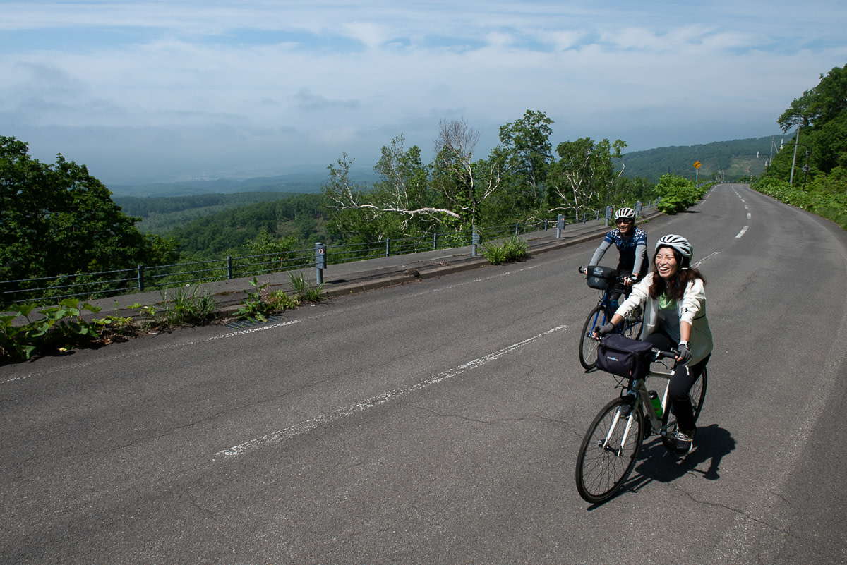 Two cyclists climb a hill with panoramic views.