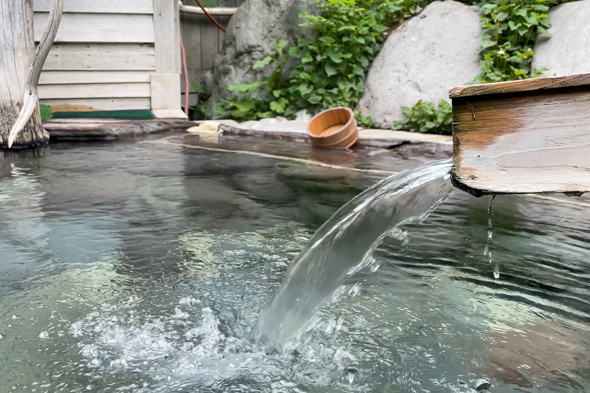 Hot-spring water gushes out of a wooden pipe and into a small outdoor bathing pool at Nukabira Onsen.