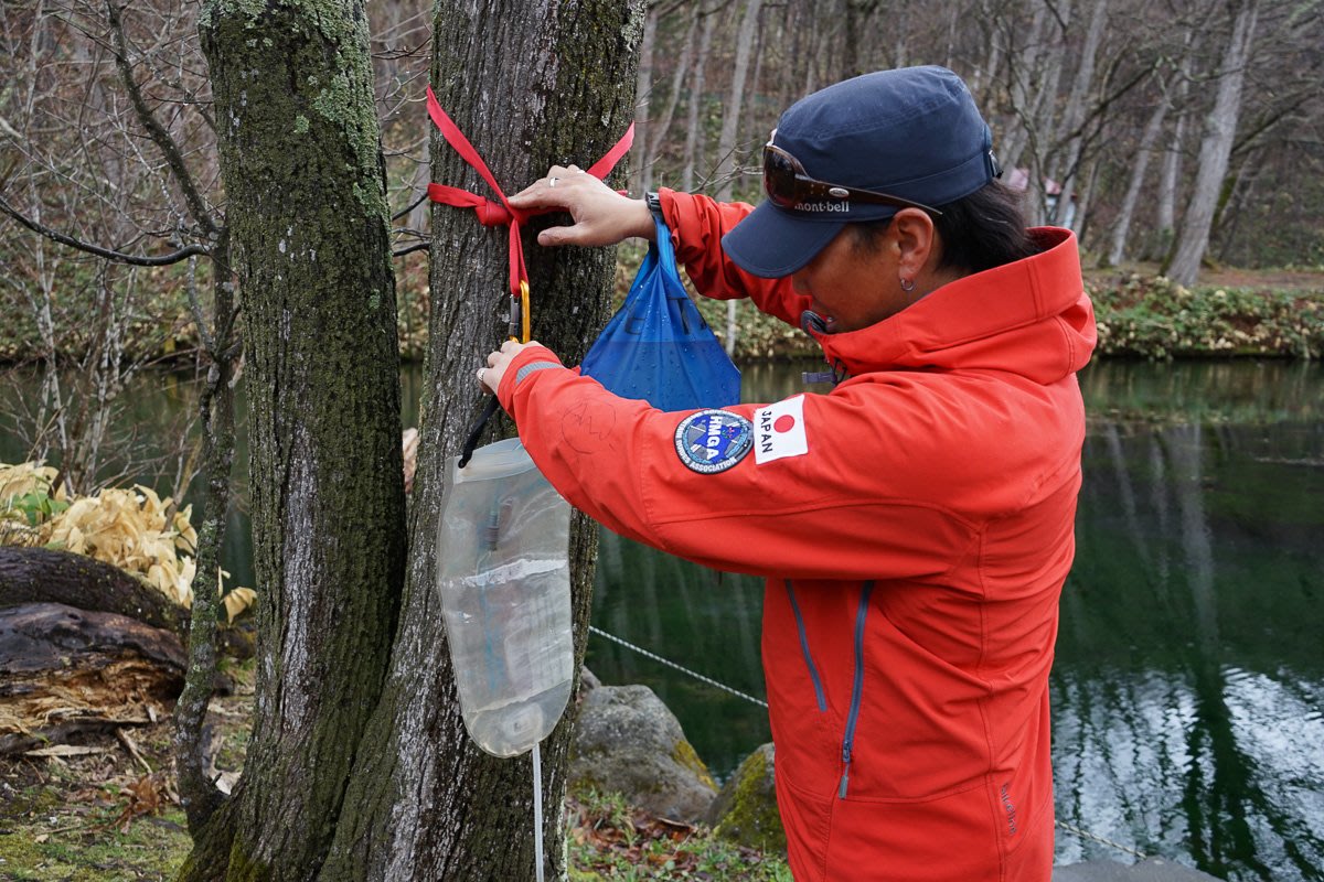 Guide filtering drinking water by hanging a plastic water bladder on a tree
