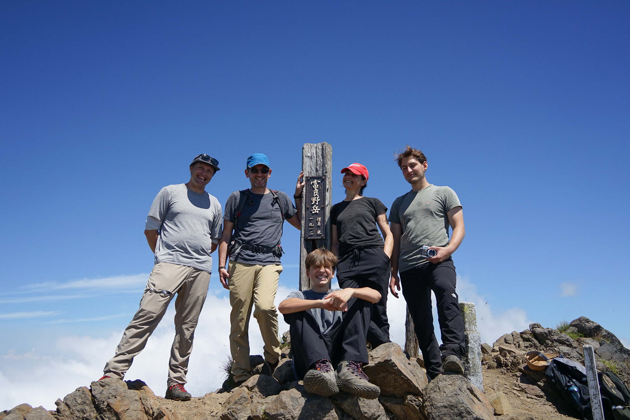 A group of hikers standing by the summit sign post of Mt. Furano under blue sky.