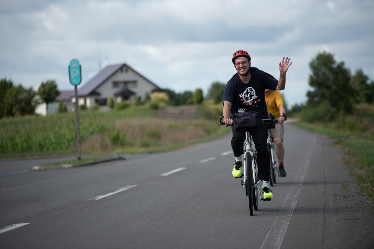 A cyclist waves as he rides along a rural road in Biei
