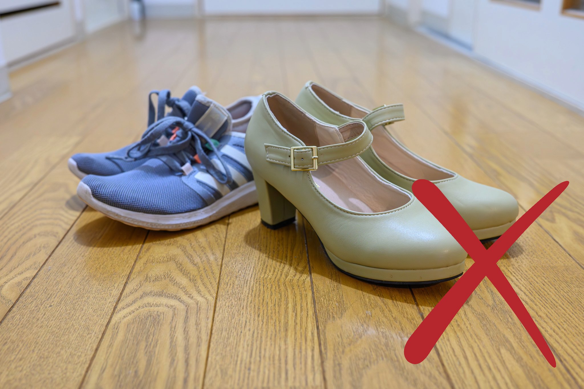 Two pairs of shoes on a wooden floor. One is a pair of heels, the other is a pair of trainers.