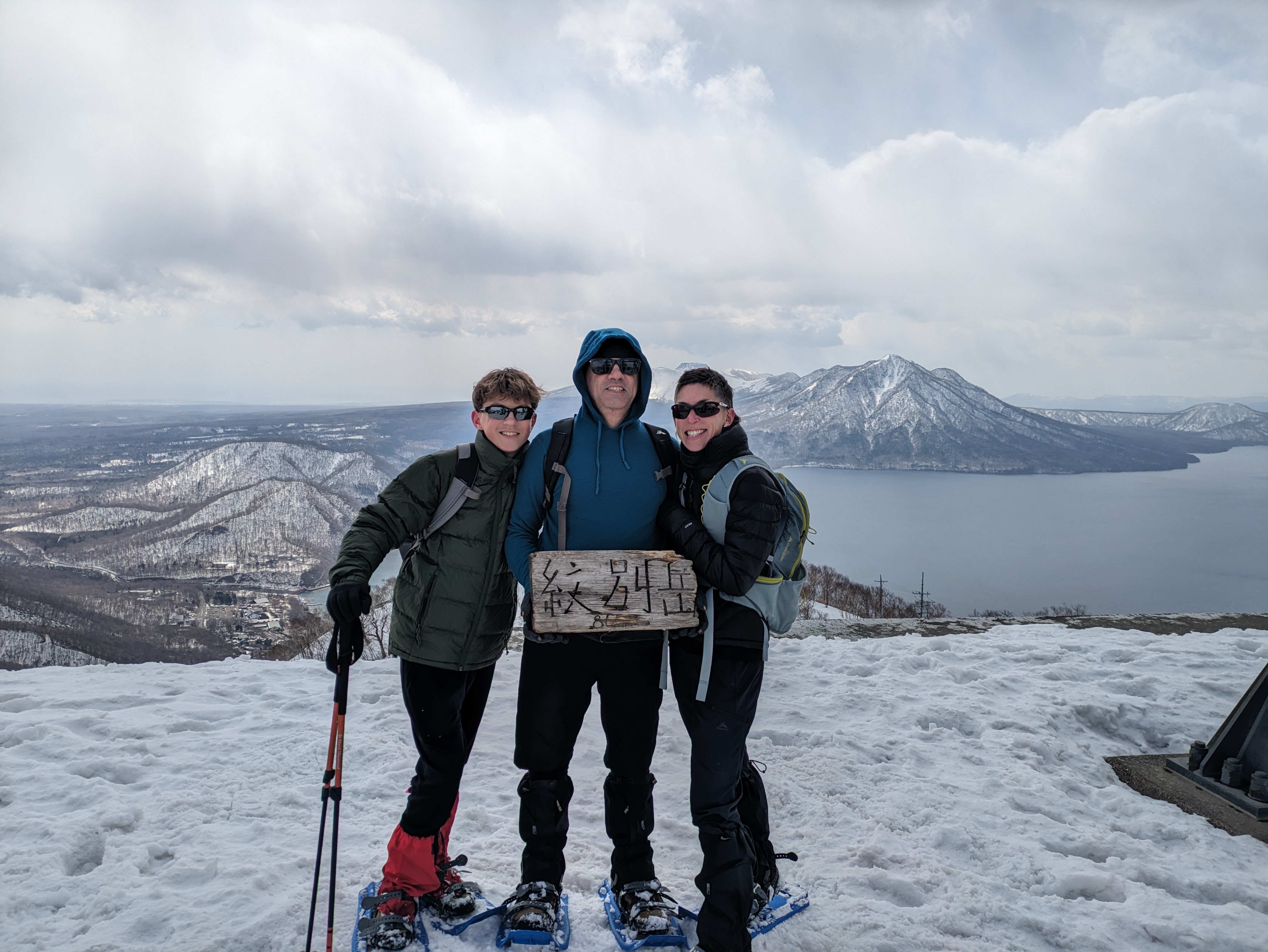 Three guests pose triumphantly at the top of Mt. Mobetsu, holding the summit sign which shows elevation.