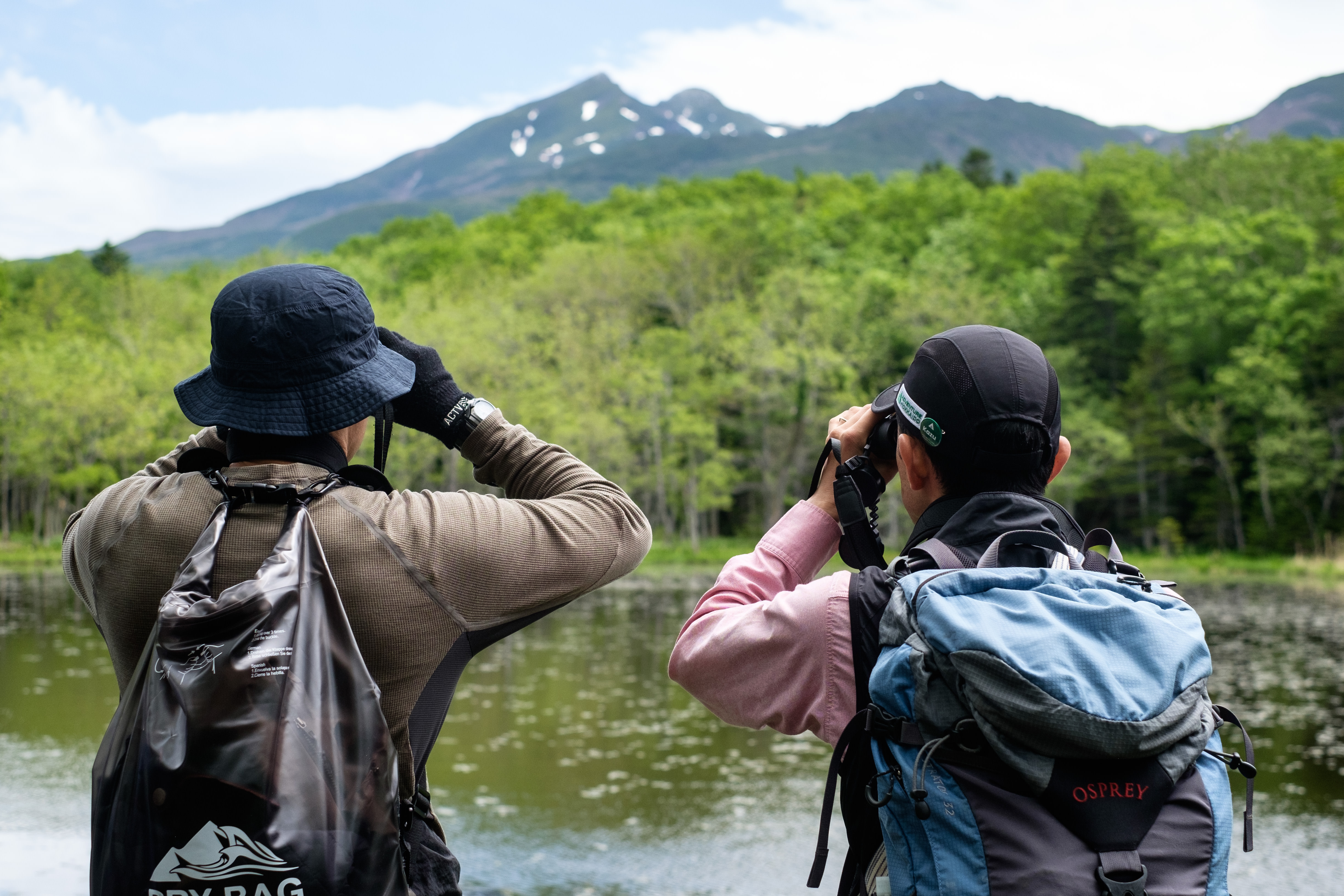 A guide and guest use binoculars to look at the last snow clinging to the mountains of the Shiretoko National Park