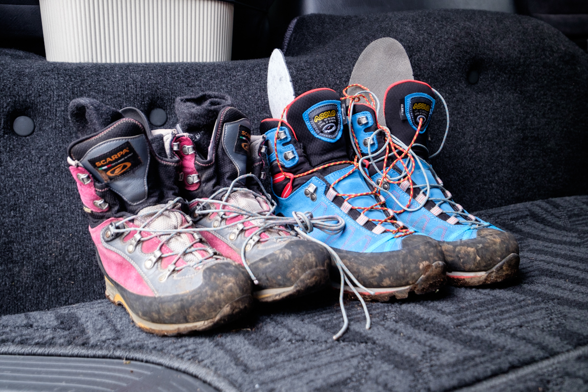 Two pairs of slightly muddy hiking boots sit on a carpet in a van.