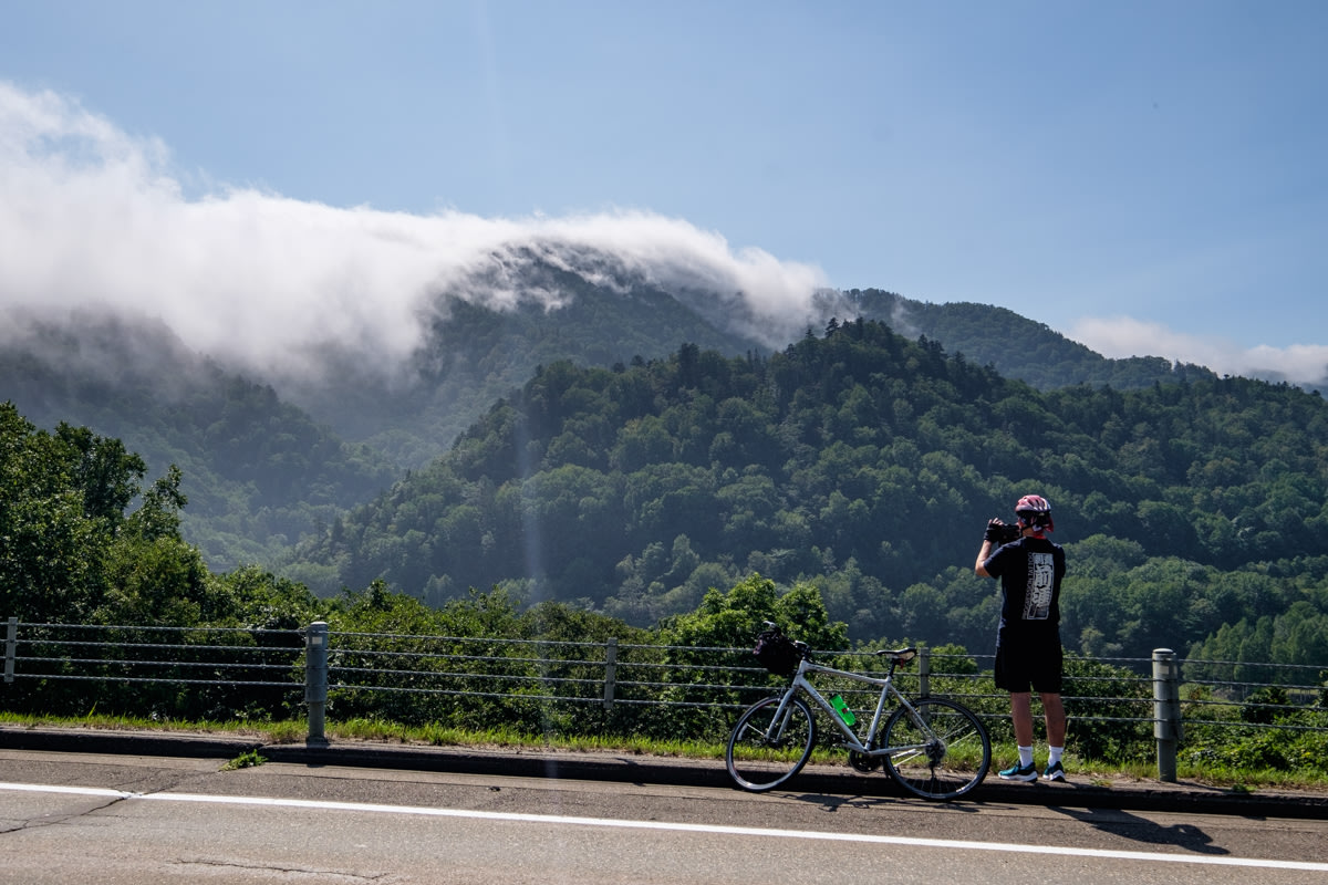 A cyclist takes a photo of a cloud capped mountain peak.