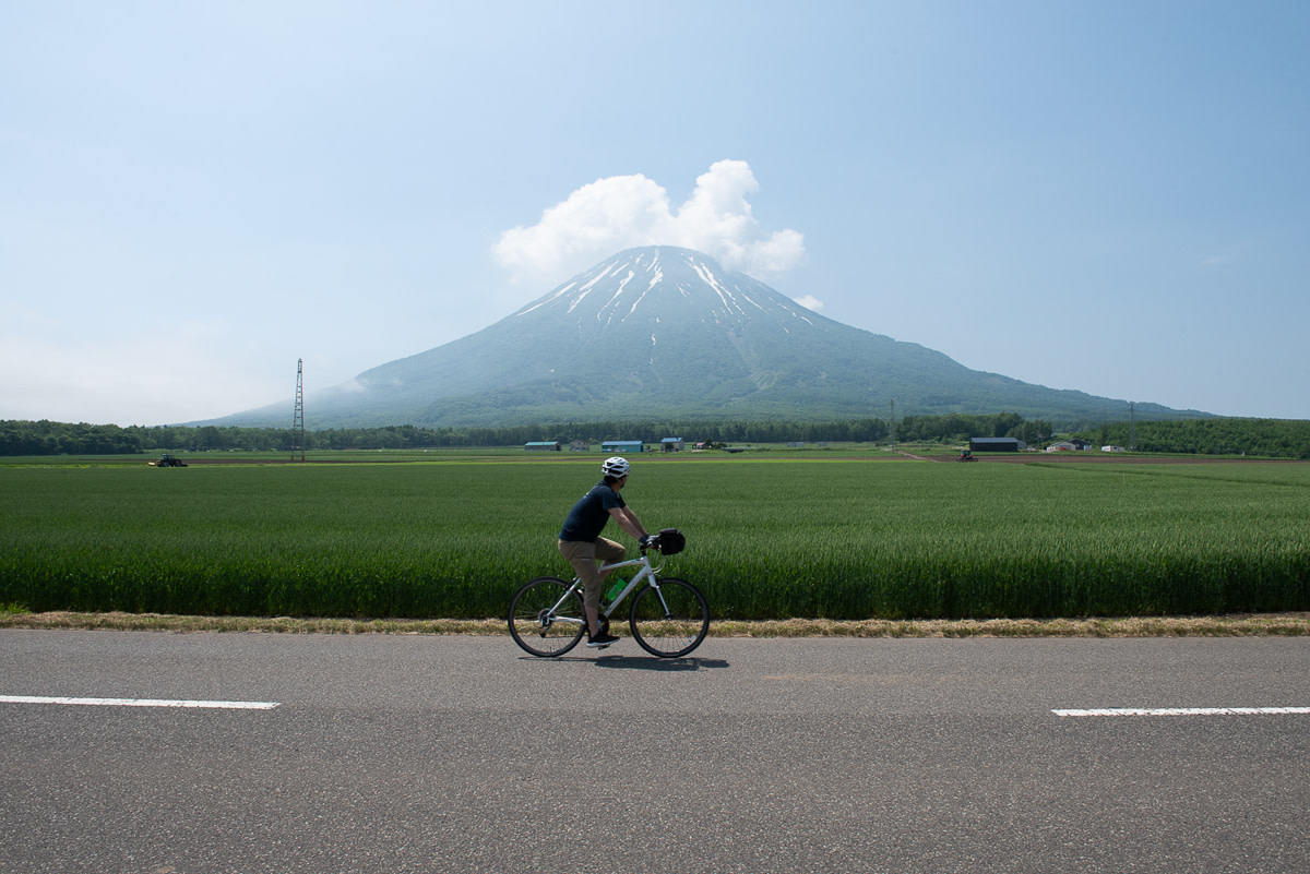 A cyclist passes by Mount Yotei, a conical volcano.
