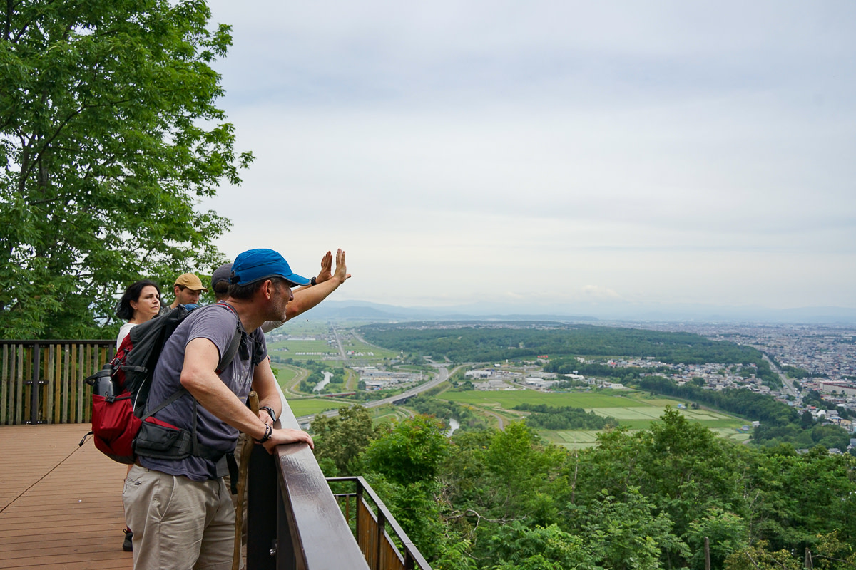 A group takes in the view of Asahikawa and the Daisetsuzan from a viewpoint above the trees