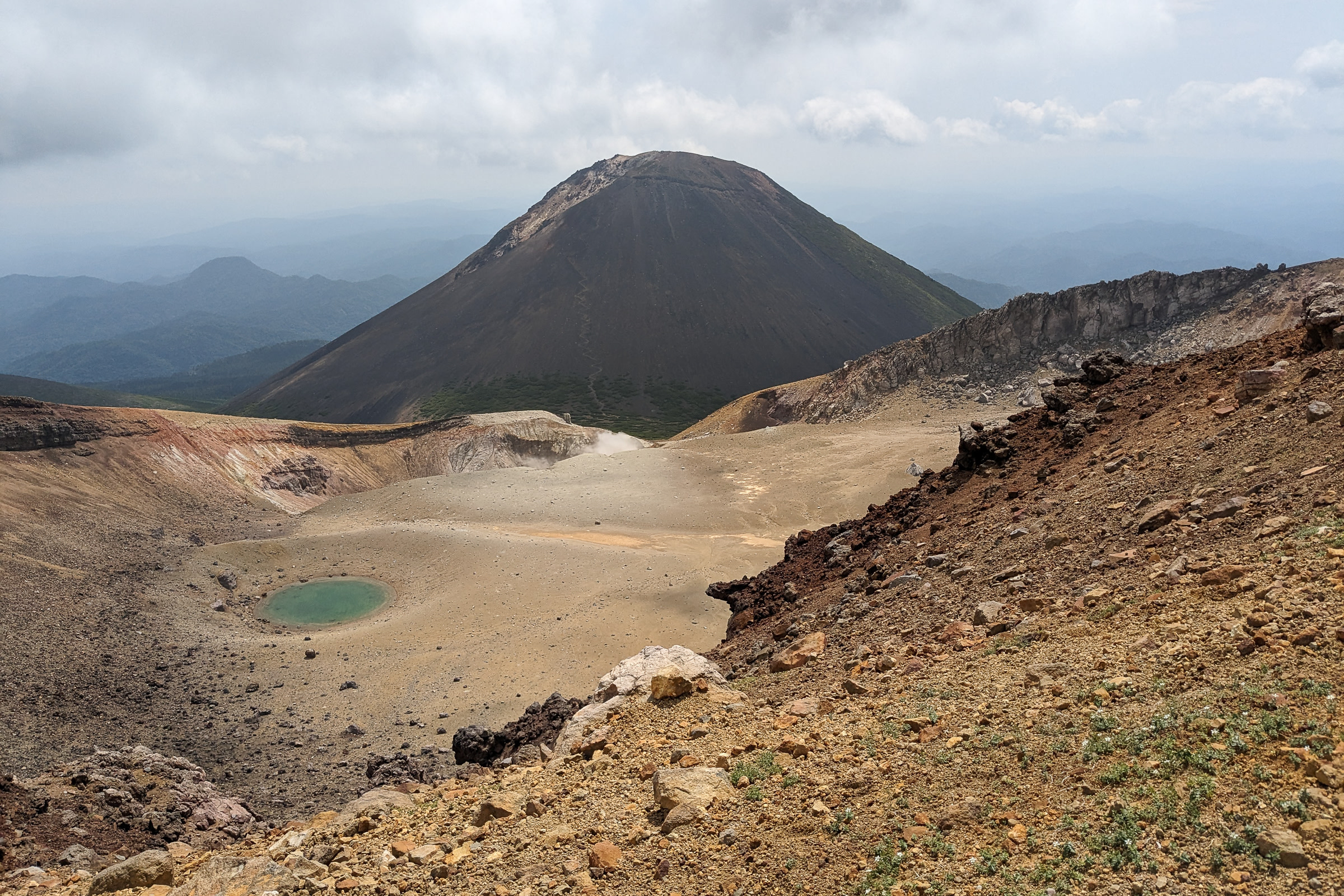 One of Mt. Meakan's crater pools looks small compared to Mt. Akanfuji's imposing figure behind it.