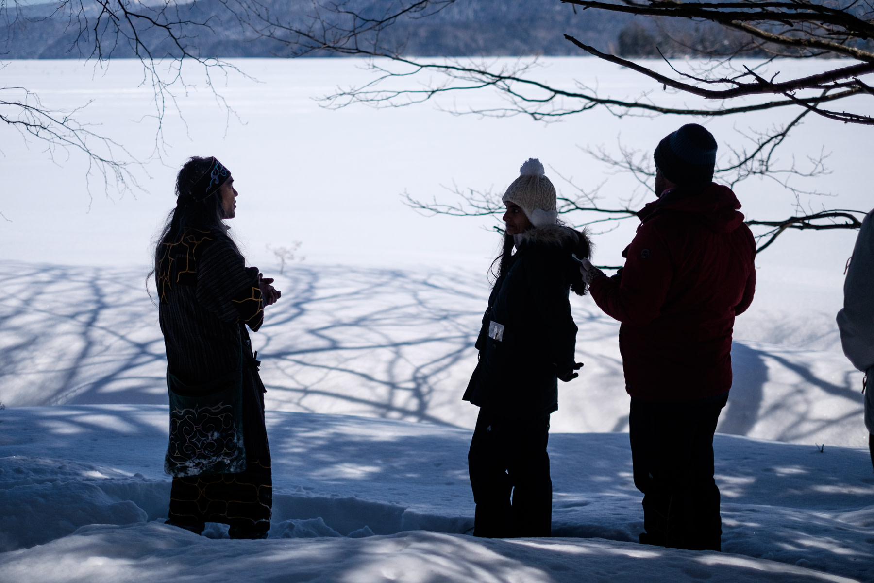 An Ainu guide and two guests are silhouetted with frozen Lake Akan in the background.