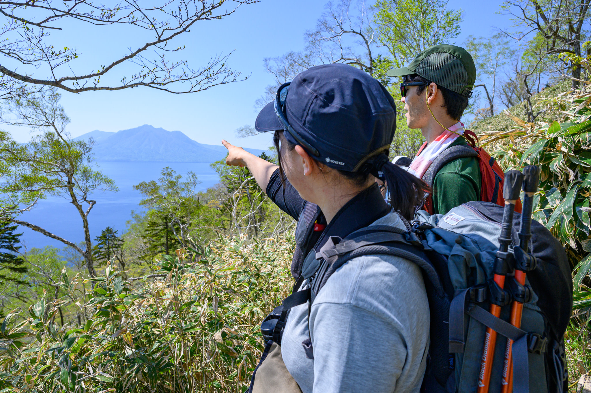 Two hikers on the trail on Mt. Ichankoppe. One of them is pointing to Mt. Fuppishi in the distance on the other side of Lake Shikotsu.