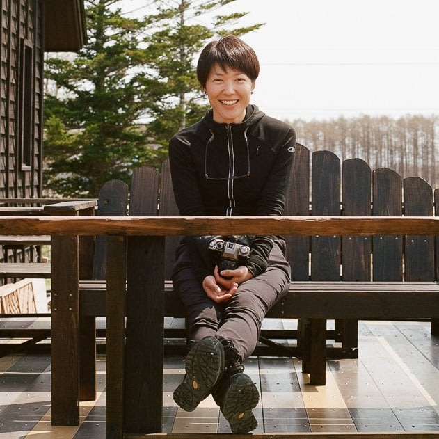 Adventure Hokkaido founder Ayaka smiles into the camera while she sits on a wooden bench located on an outside deck