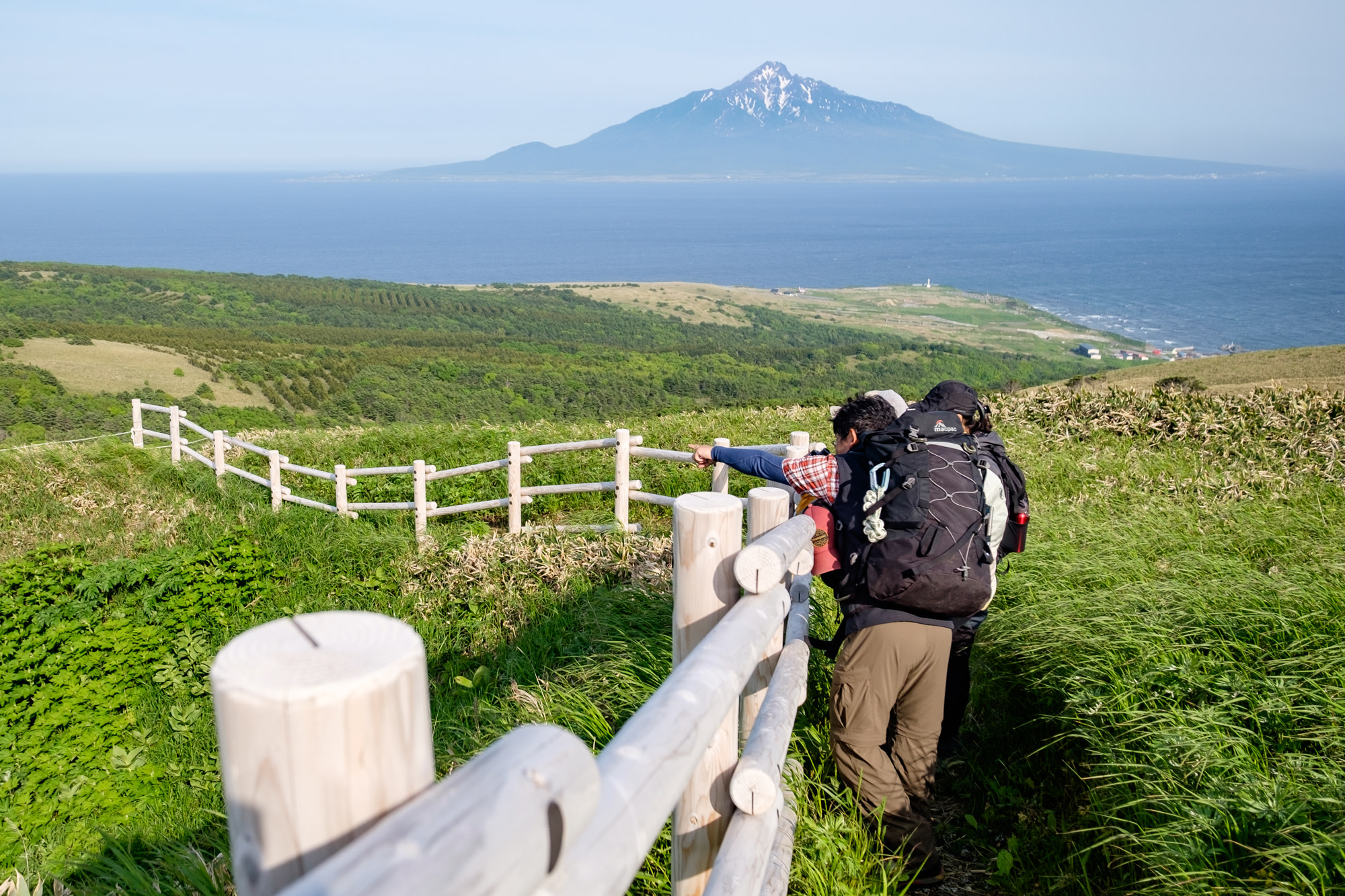 Hikers on a coastal trail with with Mount Rishiri visible across the sea