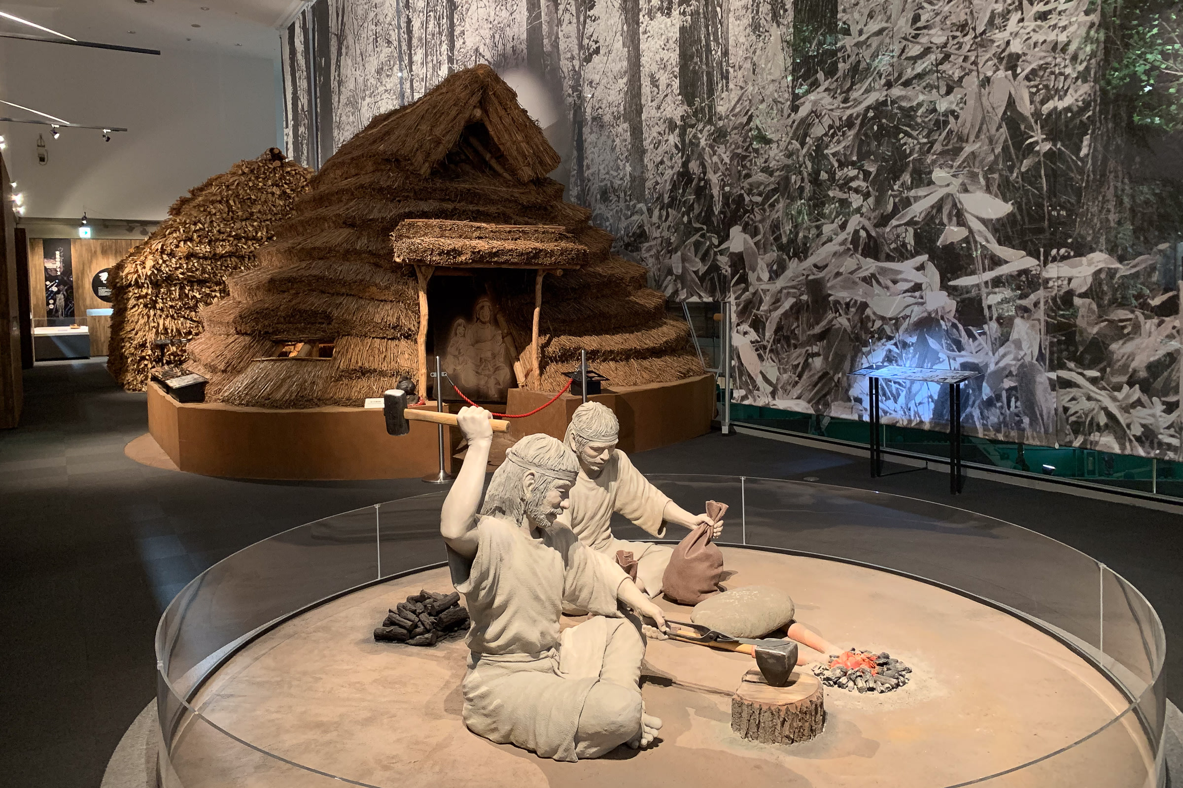 An Ainu display inside the Asahikawa City Museum. There are replica "cise", Ainu dwellings, behind two statues capturing Ainu people at work.