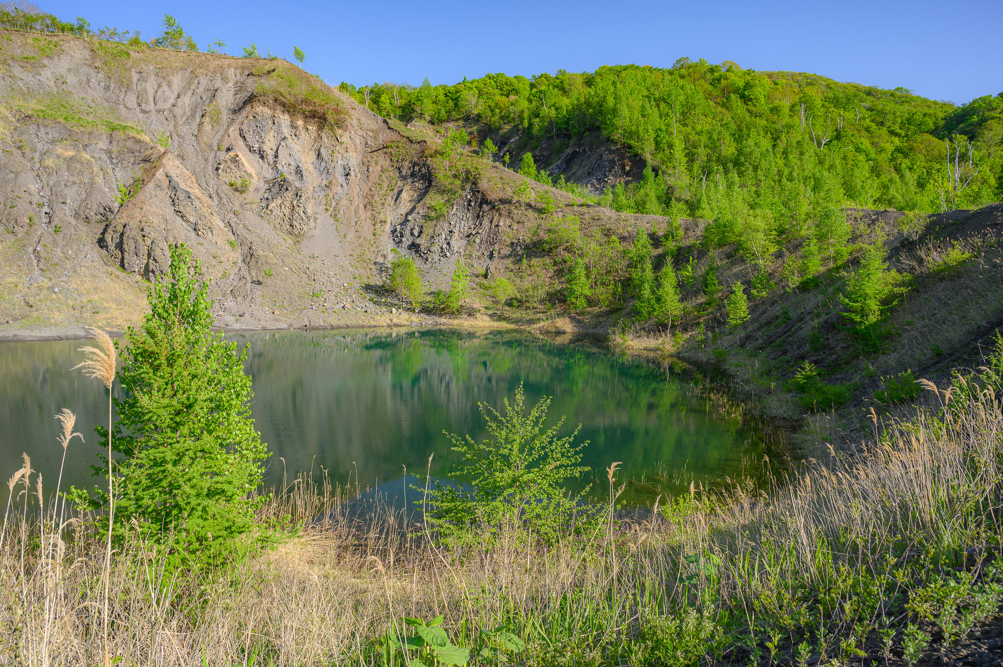 A volcanic crater lake on the Nishiyama-Kompira Trail at Lake Toya. It has steep cliffs where the ground collapsed in as a result of an eruption in 2000 and is filled with water. It is surrounded by greenery.