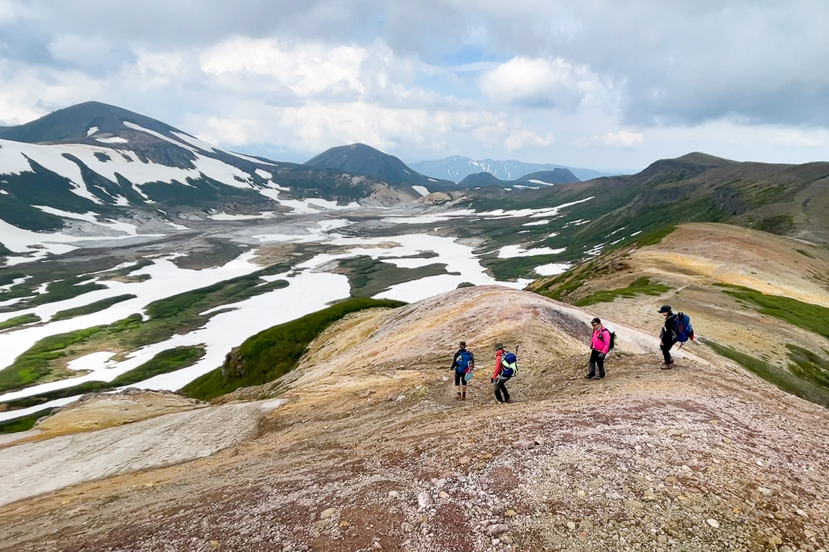 Four hikers gaze upon Daisetsuzan's Ohachidaira in summer, where large patches of snow remain.