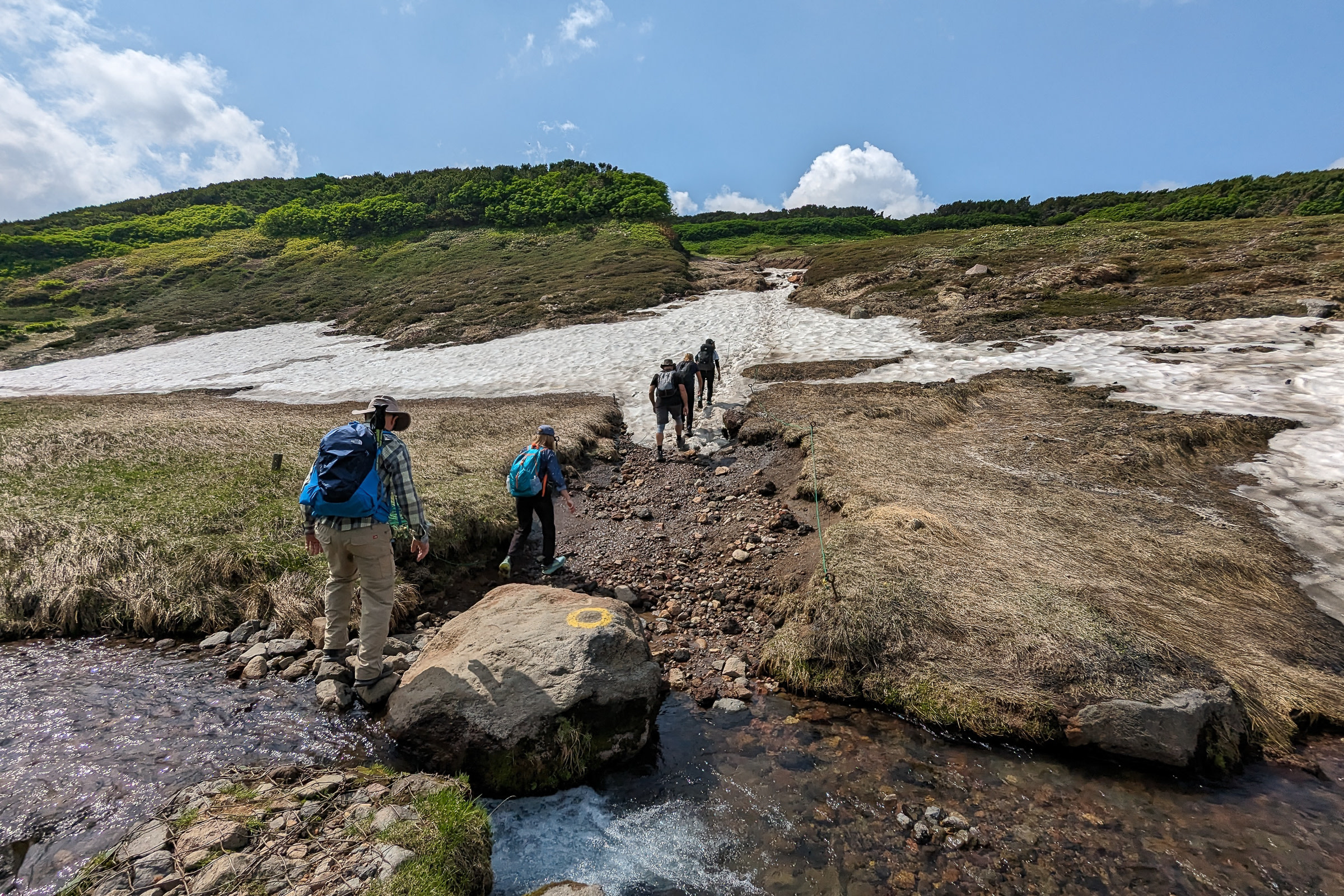 Hikers ford a shallow stream along the Asahidake-Kurodake Traverse.