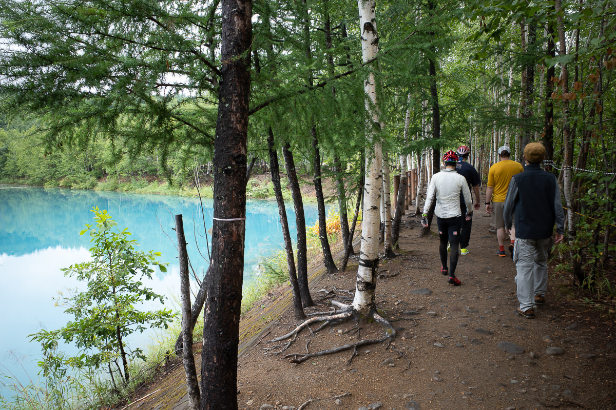 Cyclists walking alongside Biei's famous blue pond