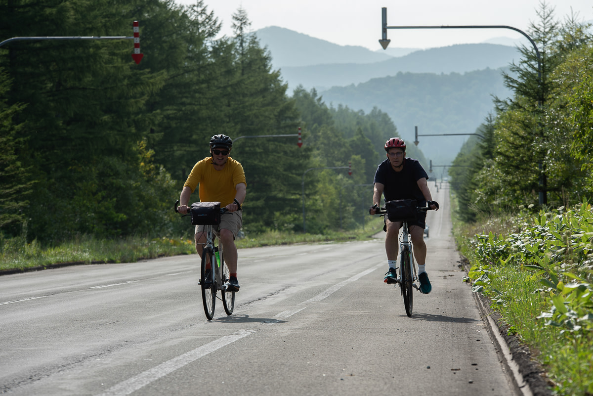 Two cyclists climb through hazy hills