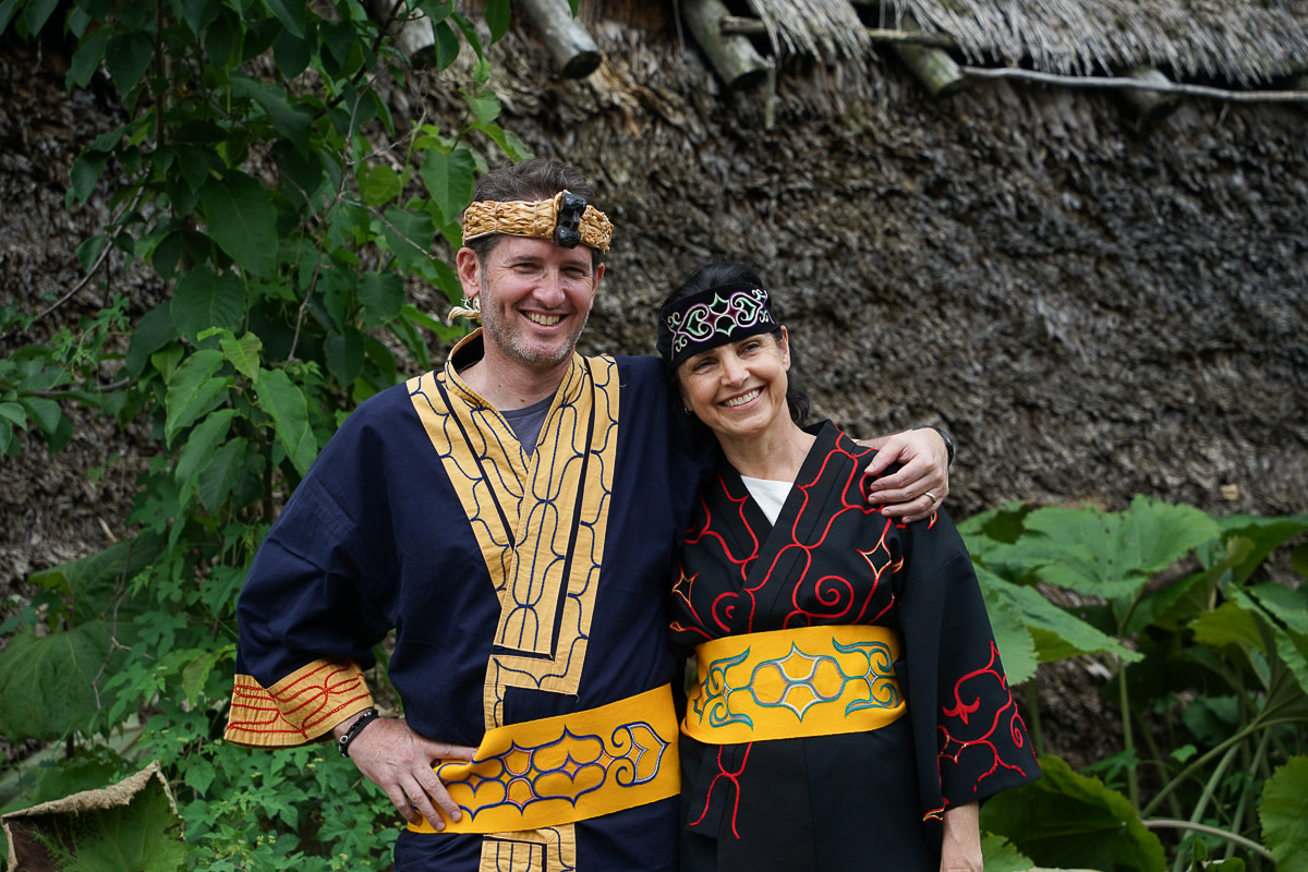 Two tourists smile as they pose in traditional Ainu clothing