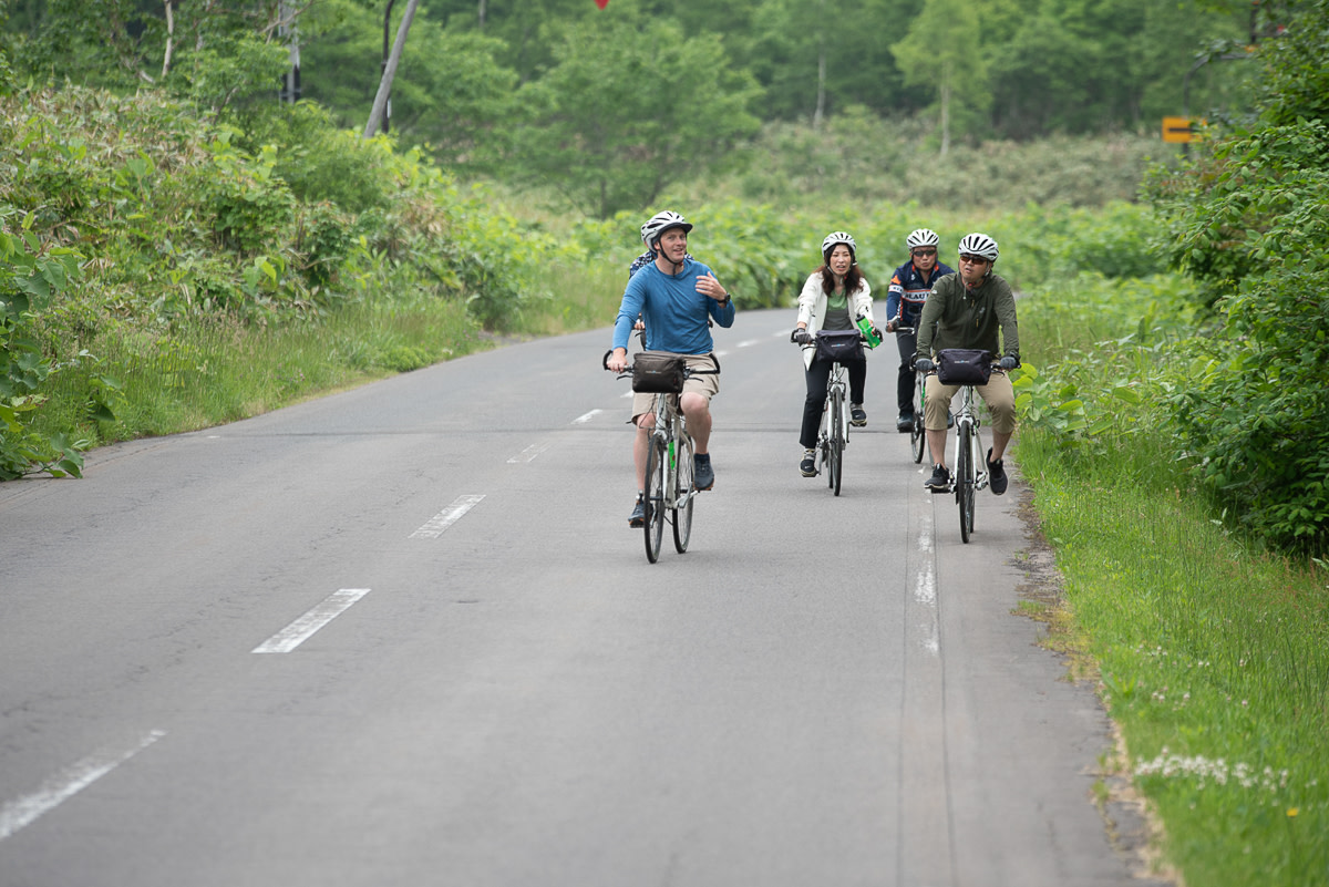A group of cyclists rides along a rural road.