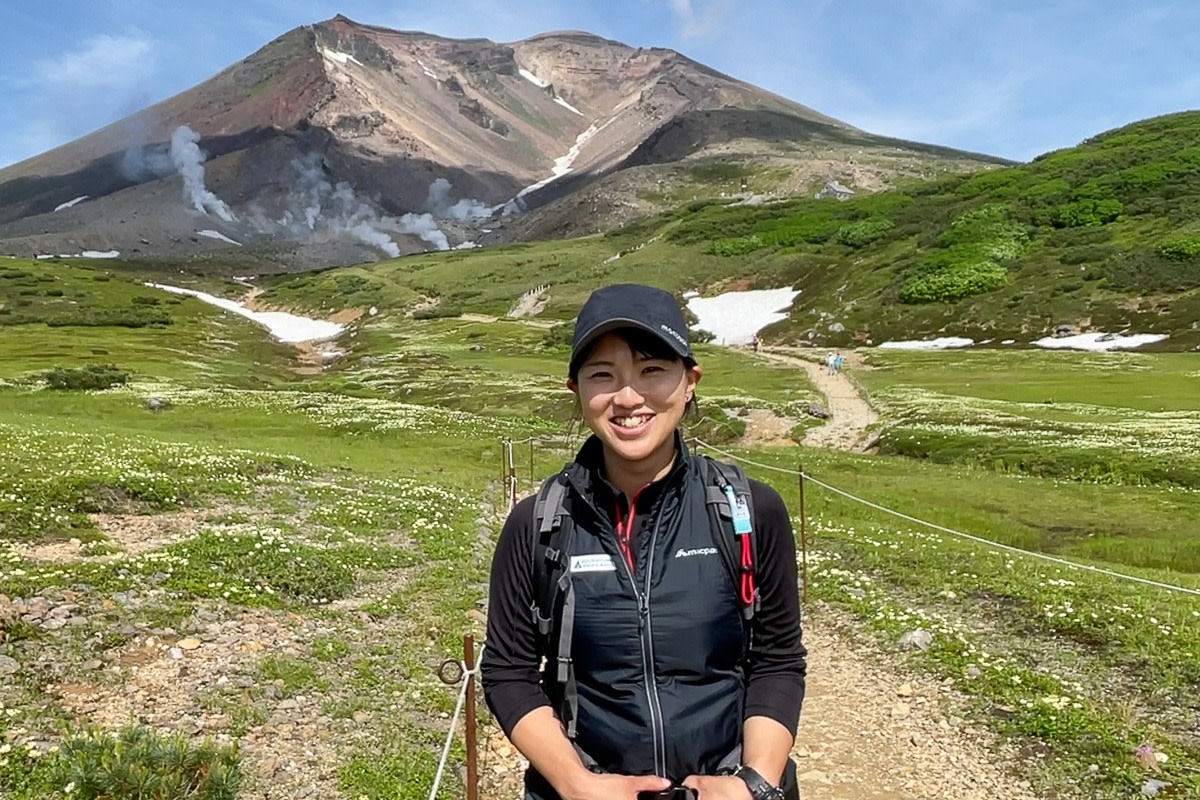 Adventure Hokkaido guide Yuka smiles at the camera while standing in front of Mt Asahidake.