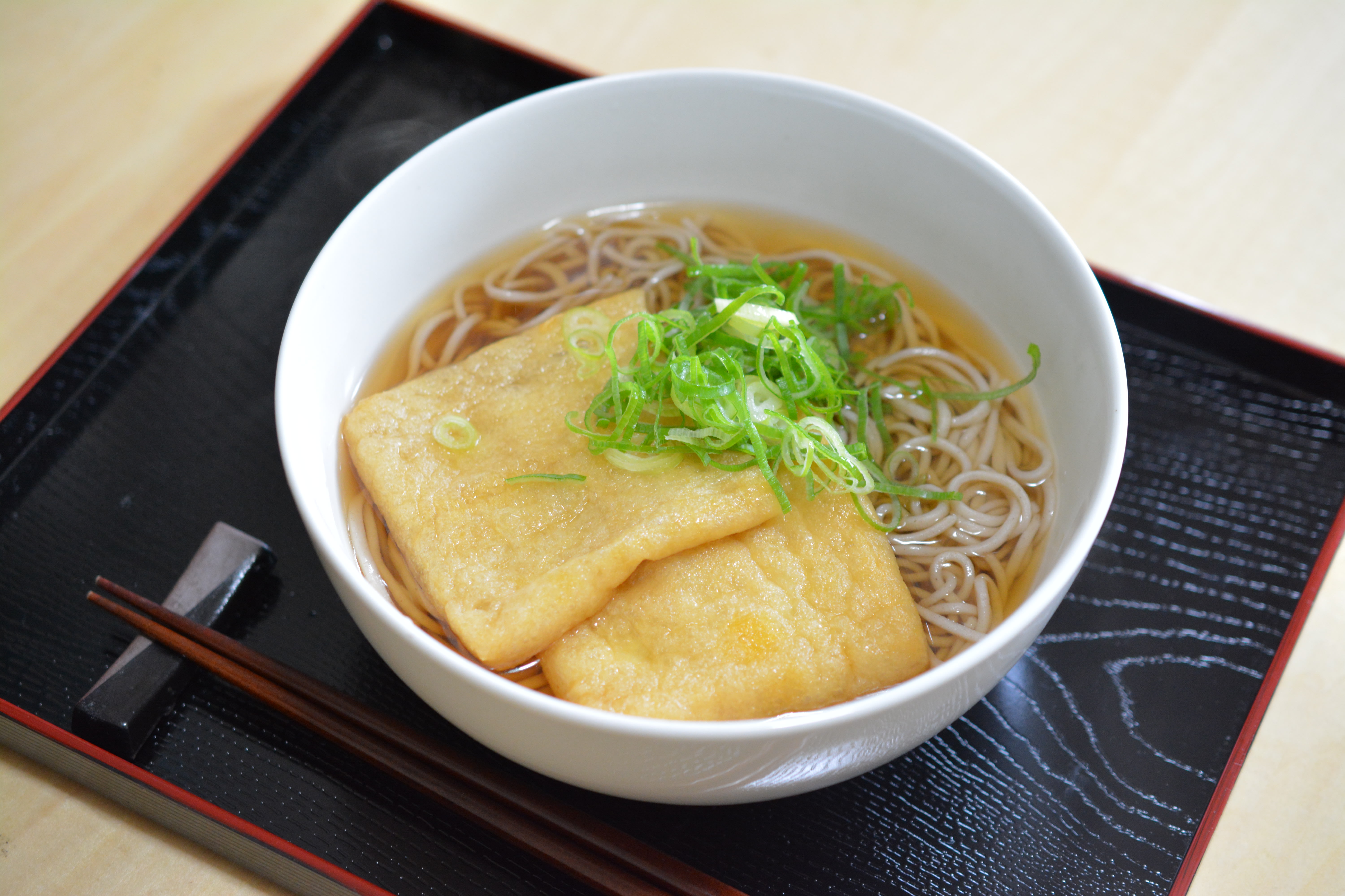 A bowl of soba (buckwheat) noodles in a bowl, topped with fried tofu skins and chopped scallions.