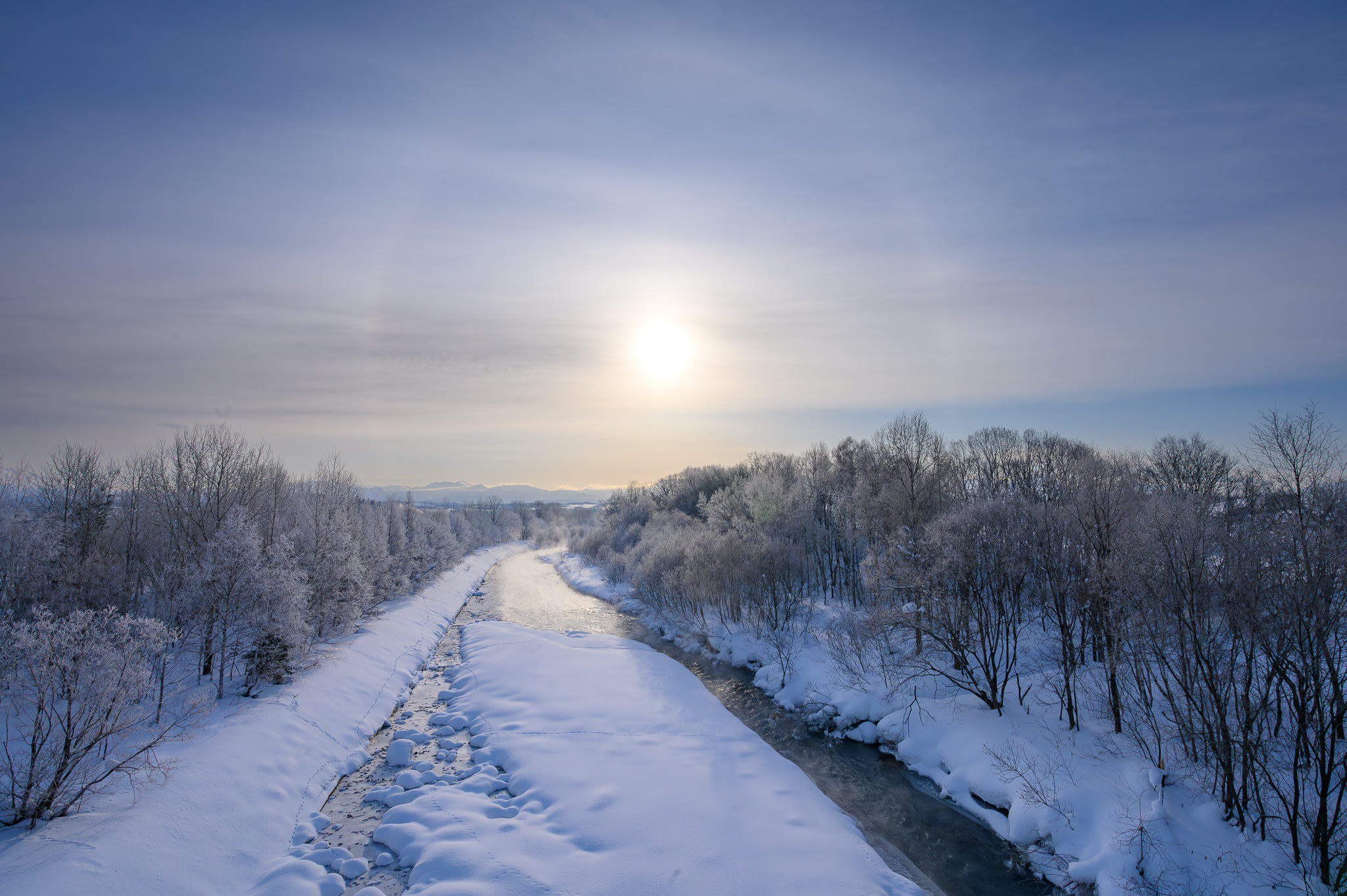 A river winds away towards the rising sun on a cold winter's morning. It is so cold that there is rime ice on the trees.