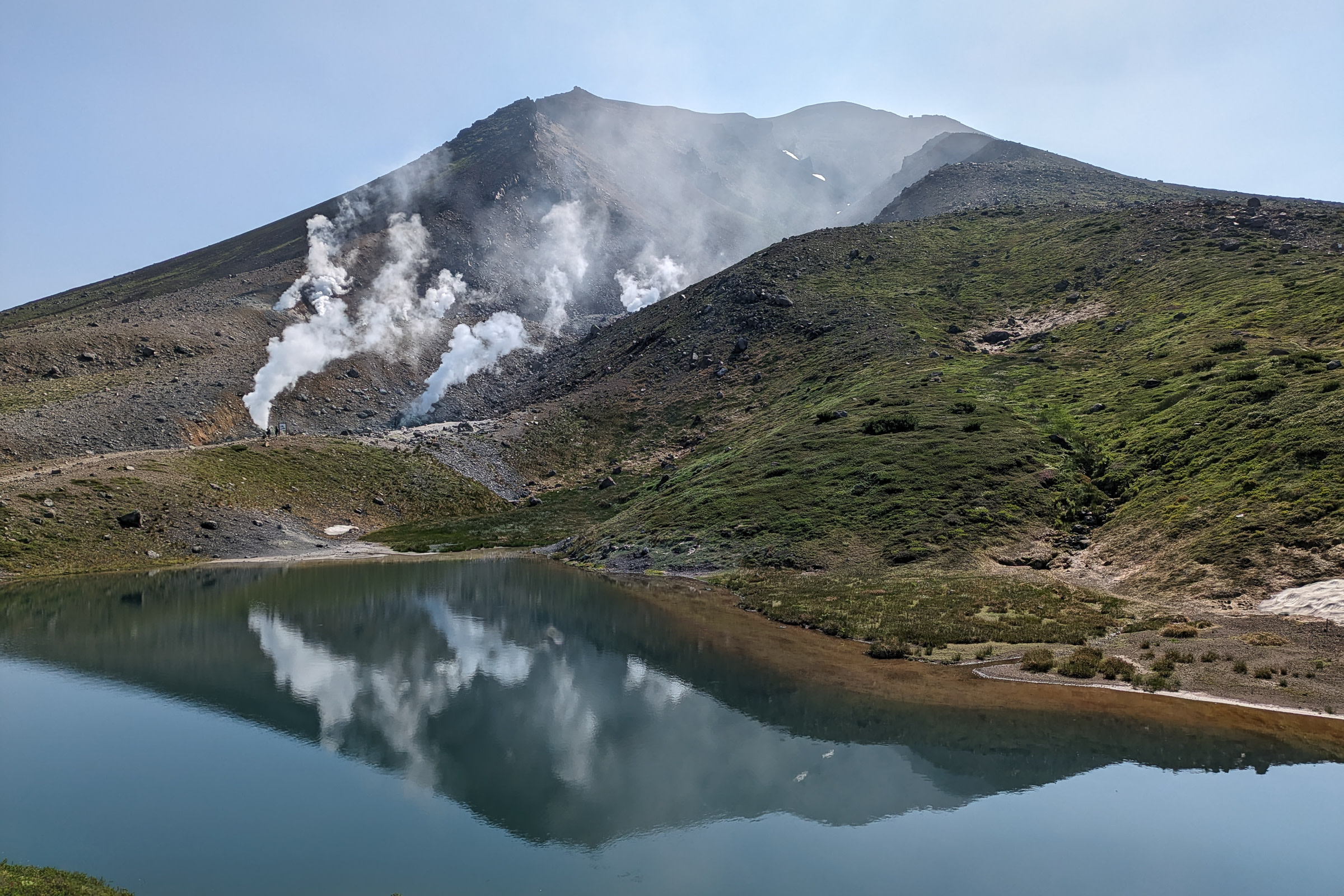 Sugatami Pond in midsummer, perfectly reflecting the cone of Mt. Asahidake in the background, smoking volcanic vents on the mountainside.