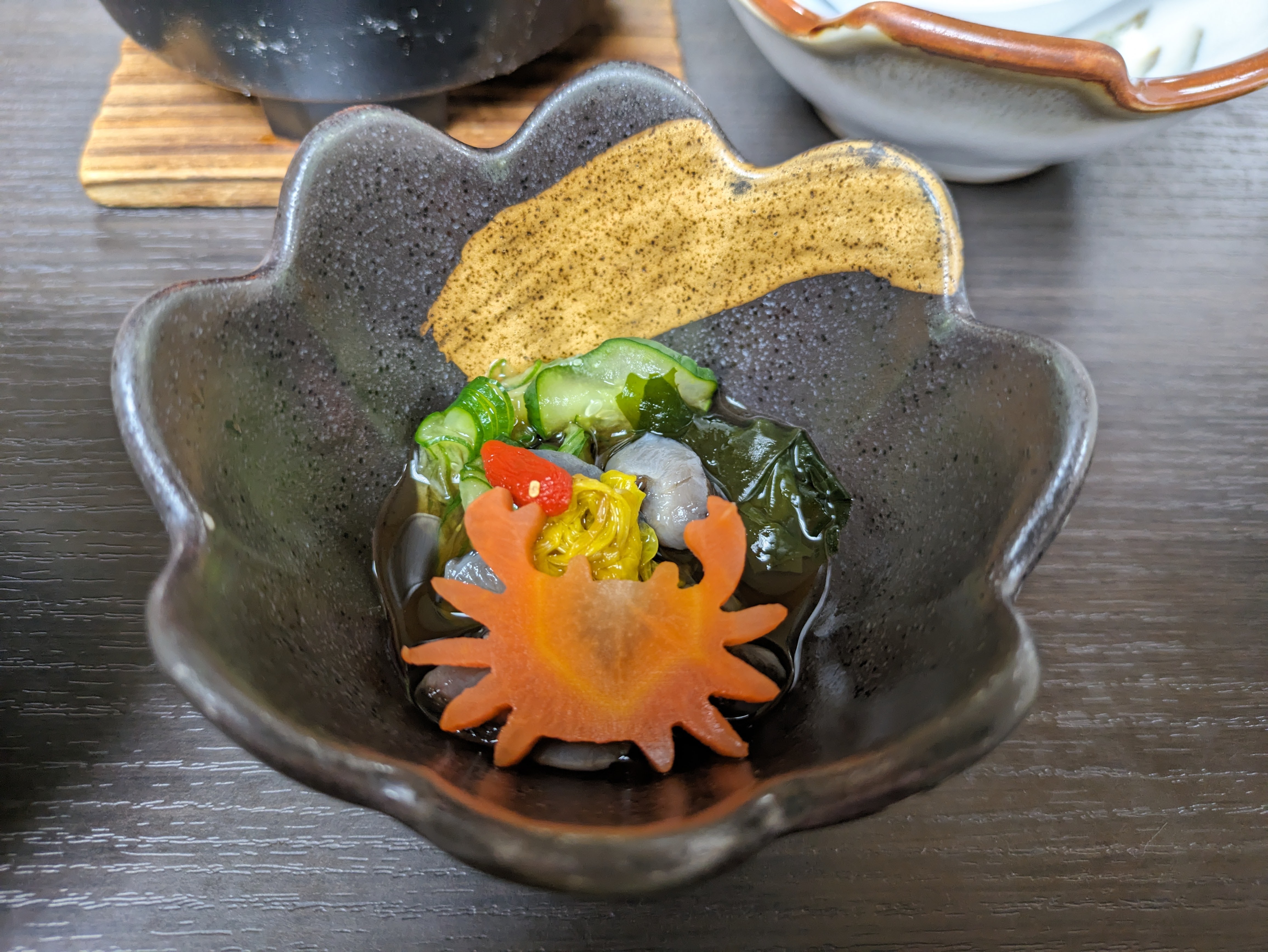 A small bowl of pickled vegetables and seafood with a slice of carrot cut into the shape of a crab.