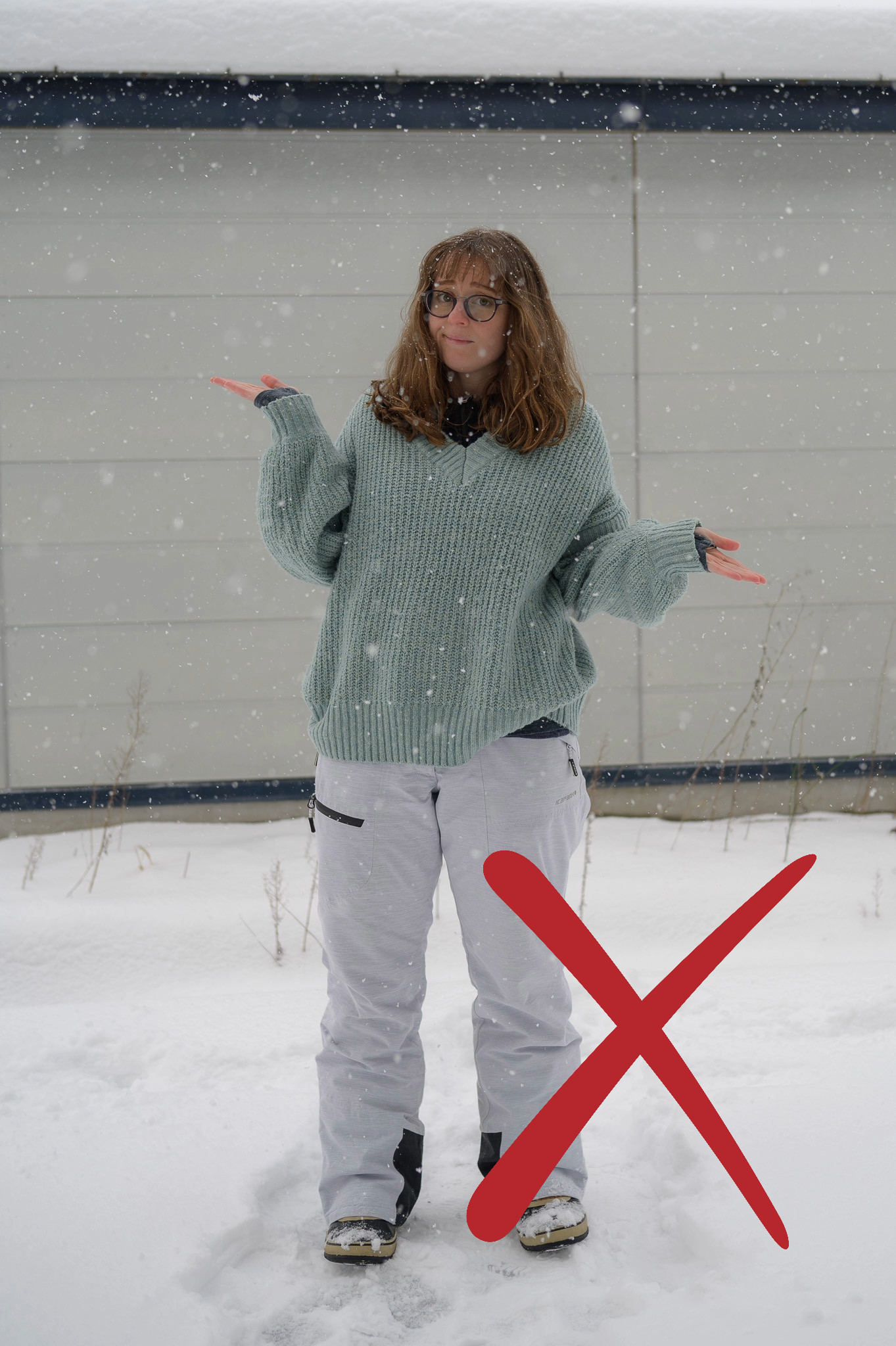 A girl wearing glasses stands in the snow wearing an oversize knitted jumper. She is shrugging.