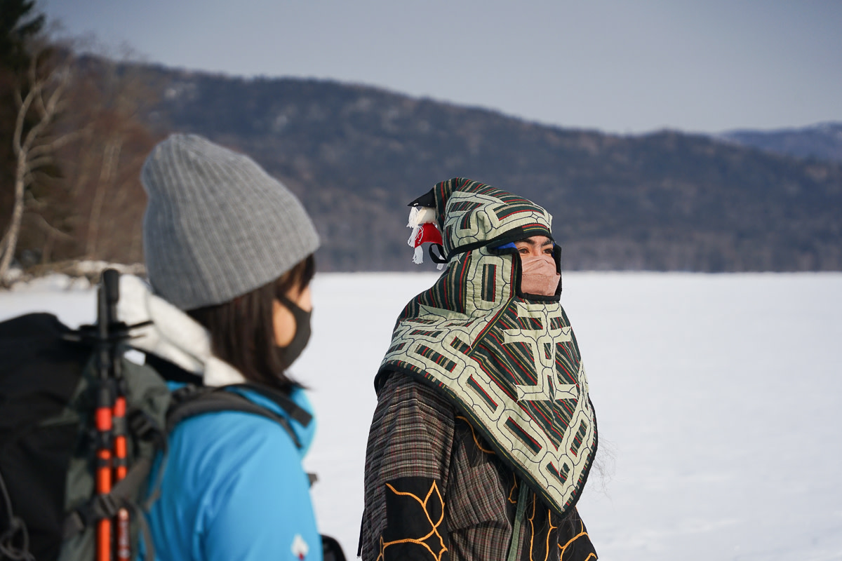 An Ainu guide wears traditional winter clothing while standing next to frozen Lake Akan