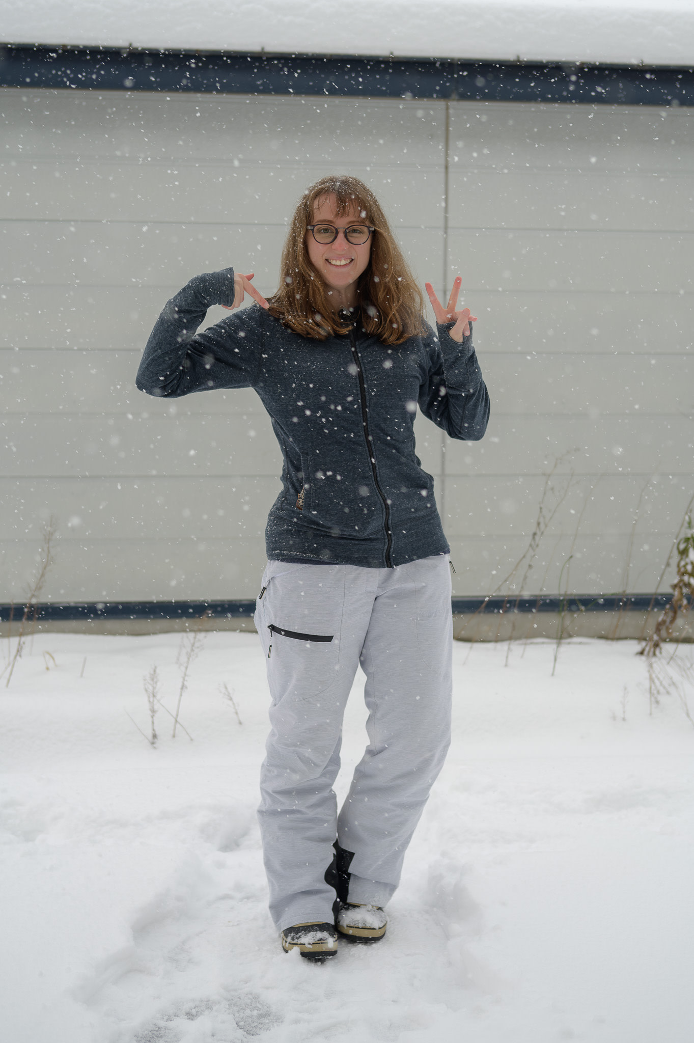 A girl with glasses stands in the snow wearing a zip-up jersey hoodie over her fleece top.