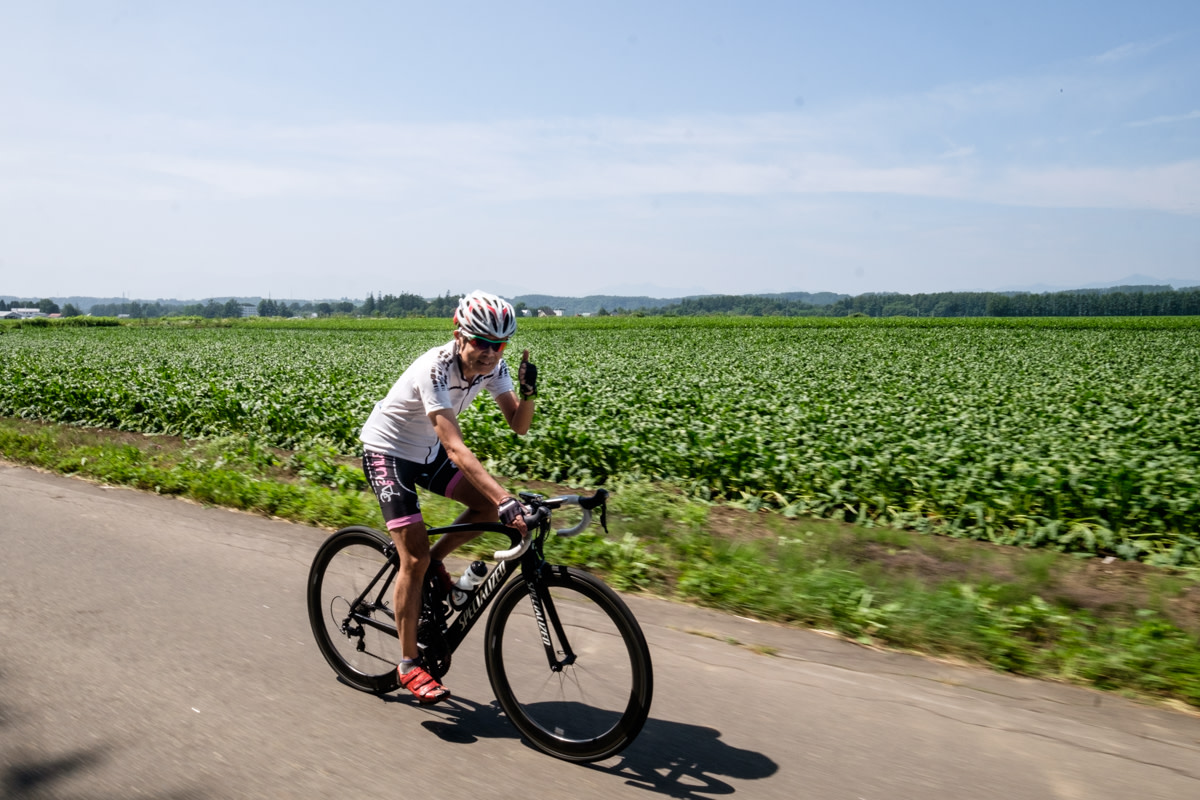A cyclist gives a thumbs up whilst riding past farmland