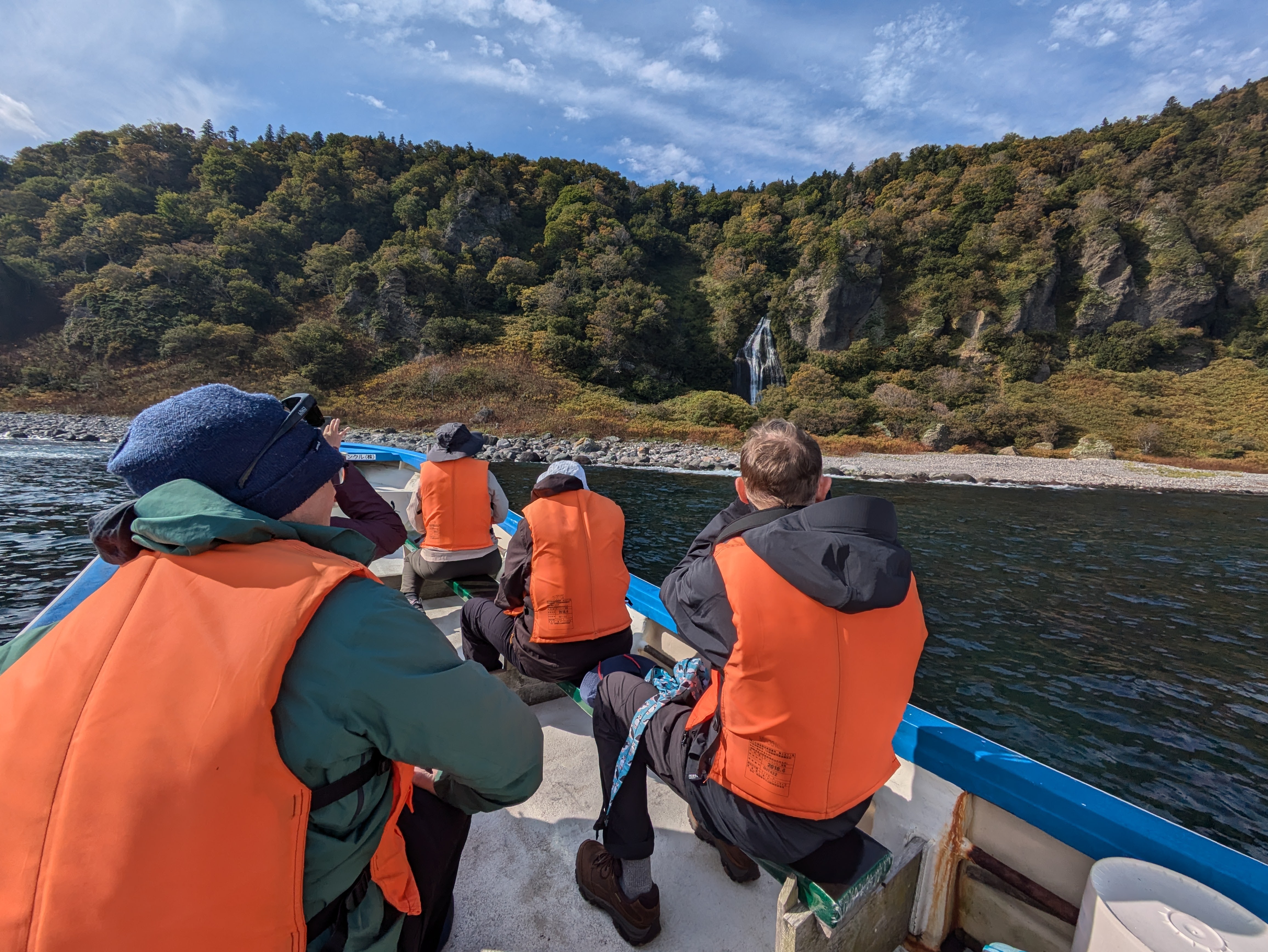 Four people on a boat out at sea look towards a waterfall on the shoreline.